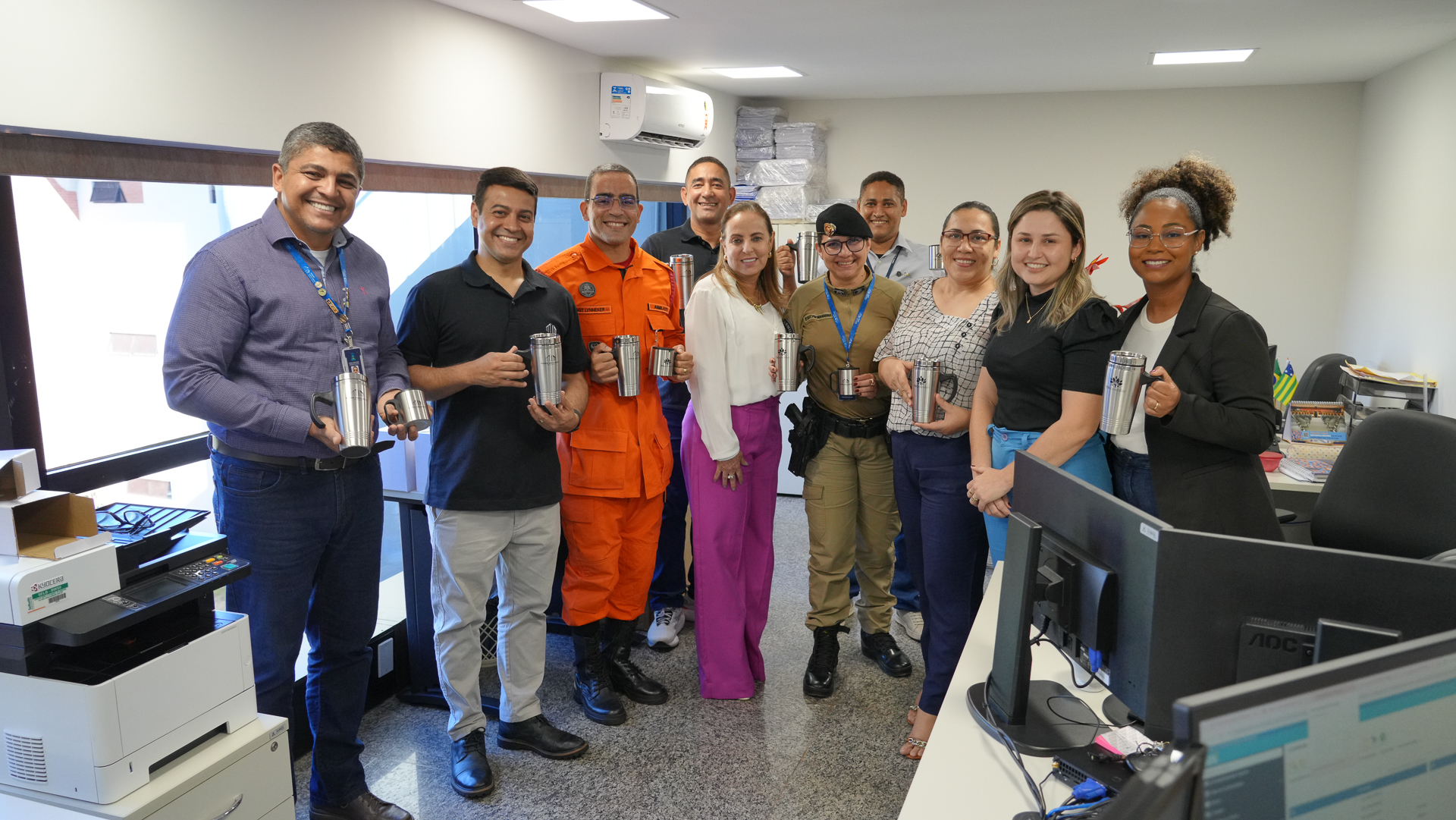 A imagem mostra um grupo de pessoas sorrindo e posando para a foto em uma sala. Cada pessoa segura o kit de sustentabilidade entregue pela desembargadora Ângela Prudente. Os kits, formados por uma caneca e um copo de alumínio, integram a campanha “Meu Copo, Meu Ambiente”, do Tribunal de Justiça do Tocantins, que busca reduzir o uso de materiais descartáveis no Judiciário.