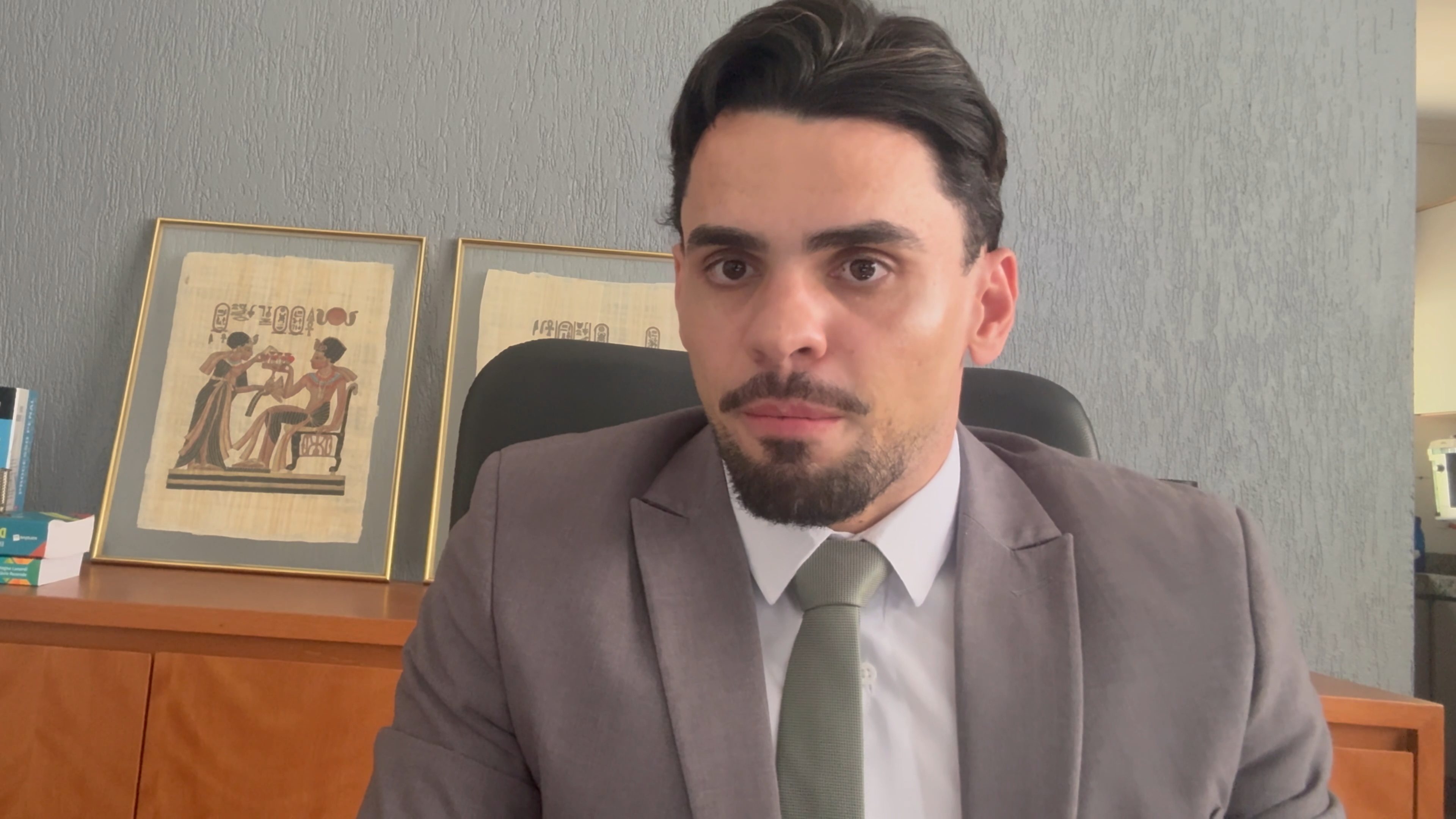 Promotor de Justiça Jorge; homem de pele clara, cabelos e cavanhaque escuros; ele usa camisa branca e terno e gravata cinza