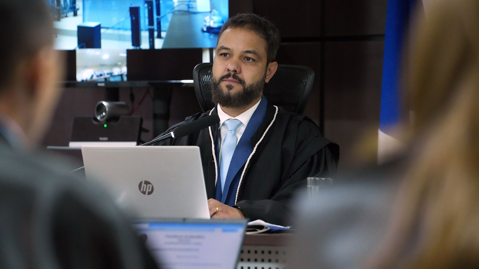 Juiz Cledson Nunes, de terno, camisa branca, gravata azul e uma toga por cima durante audiência