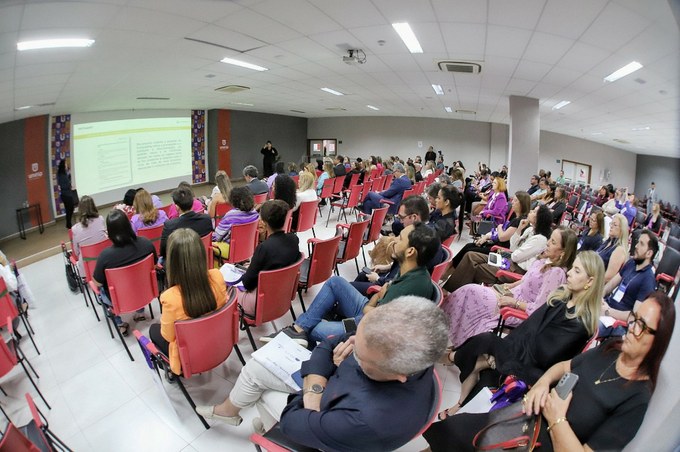 A imagem mostra a abertura do 2º Encontro Nacional Ouvir e Enfrentar (ENOE), promovido pelo Tribunal Regional do Trabalho da Paraíba. A sala está cheia, com pessoas sentadas em cadeiras vermelhas, acompanhando uma apresentação.
