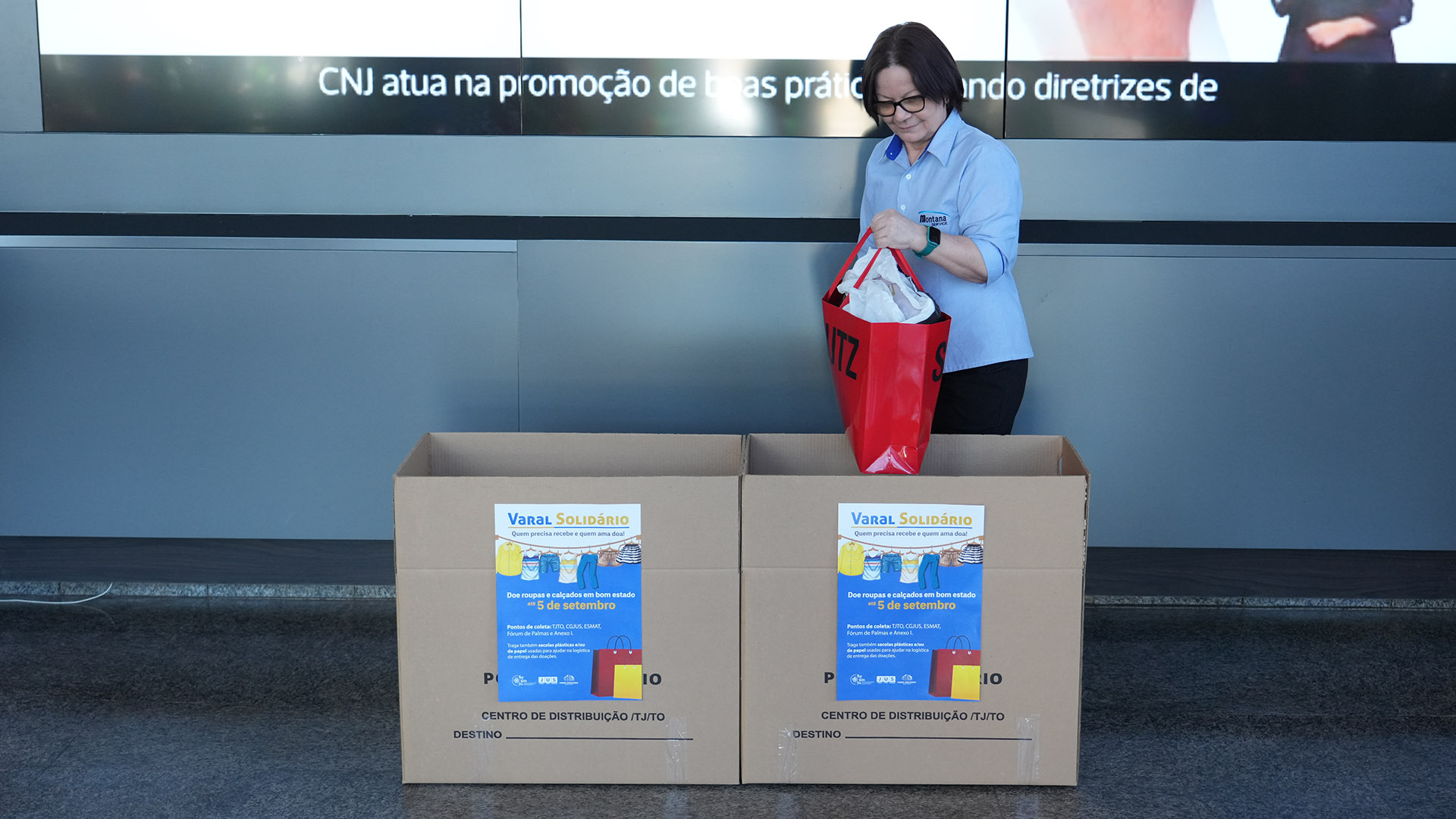 A imagem mostra uma mulher entregando uma sacola com roupas para a campanha Varal Solidário do Poder Judiciário.