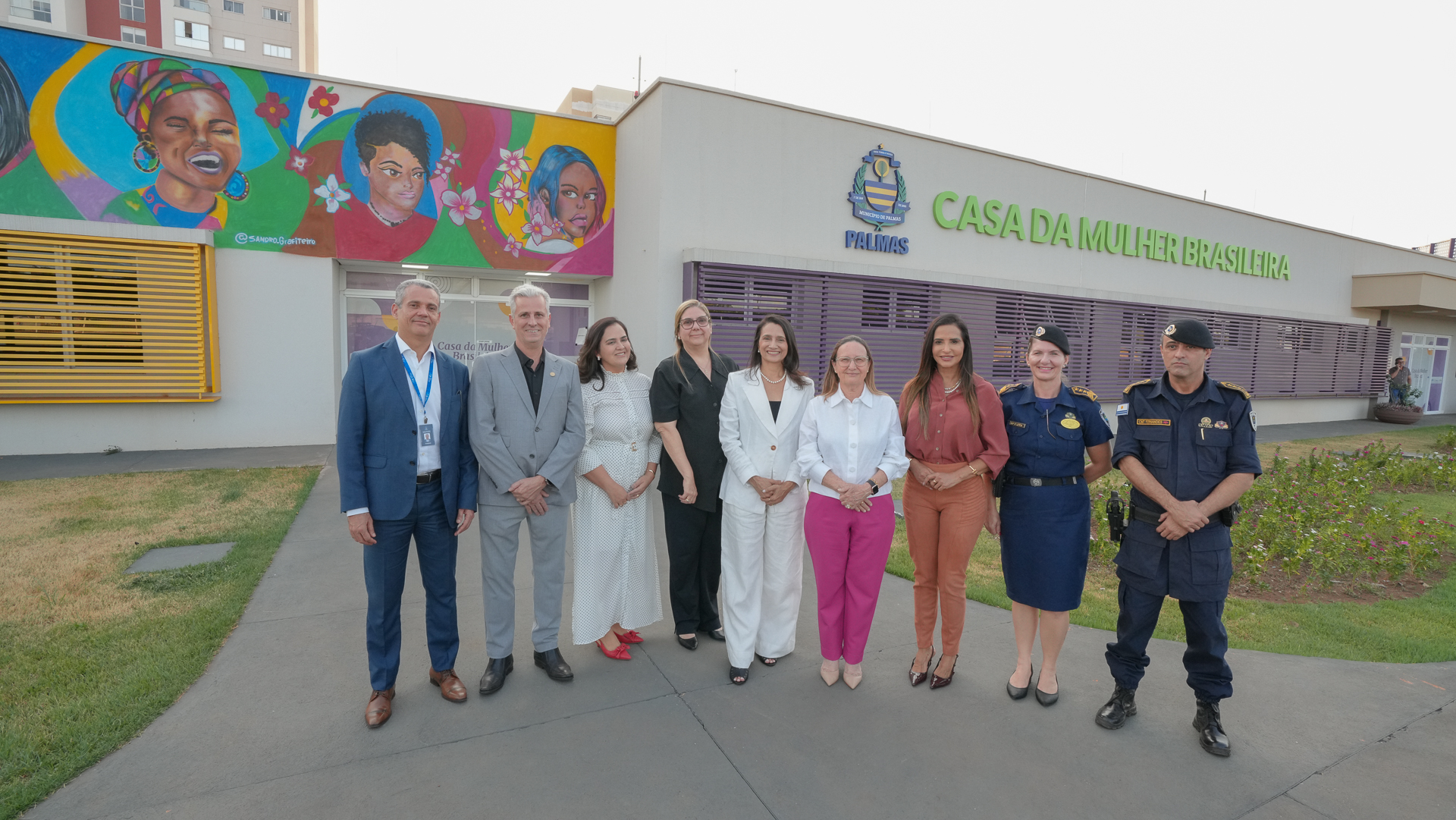 Homens e mulheres em pé durante foto posada em frente a espaço de atendimento à mulher vítima de violência doméstica