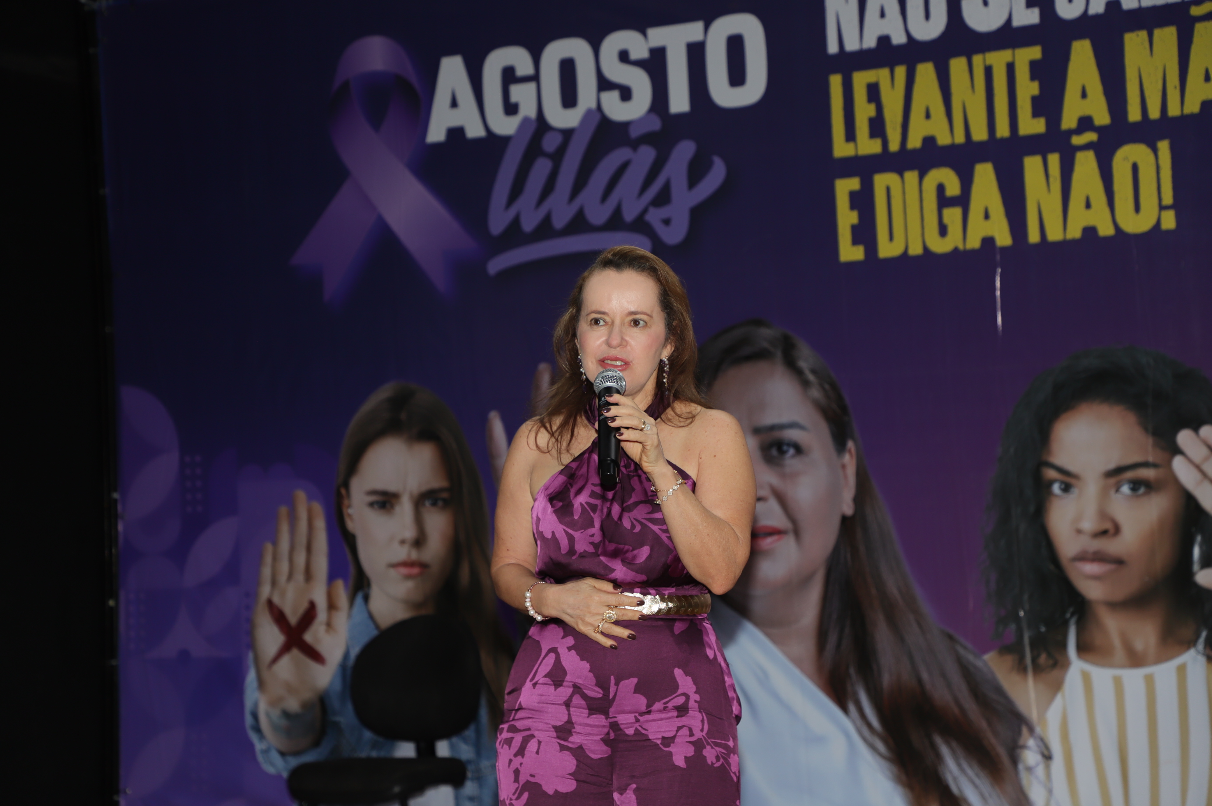 Juíza Cirlene fala ao microfone durante evento; ela é uma mulher de pele clara e usa roupa em tons de roxo e lilás