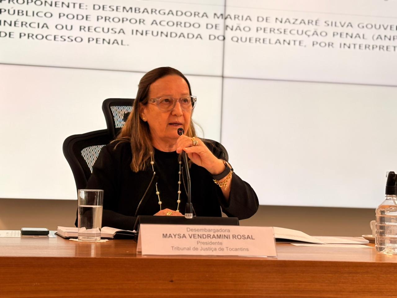Desembargadora Maysa Vendramini Rosal, presidente do Tribunal de Justiça do Tocantins, está em um evento; ela está sentada à mesa, falando em um microfone.