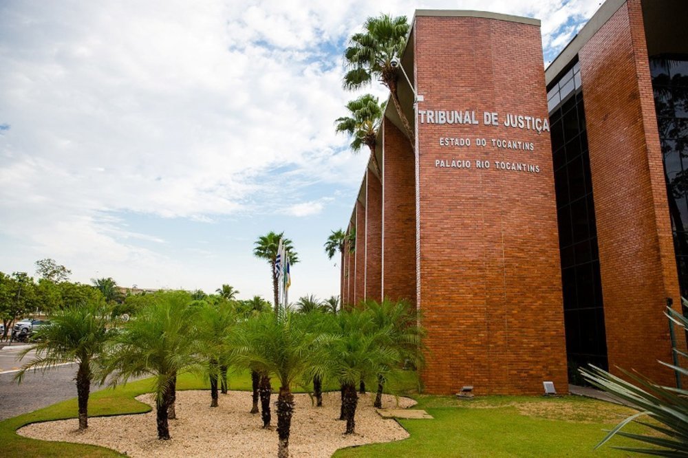 mostraA imagem mostra a fachada do Tribunal de Justiça do Estado do Tocantins, um edifício em tijolos aparentes, sob um céu azul ensolarado.