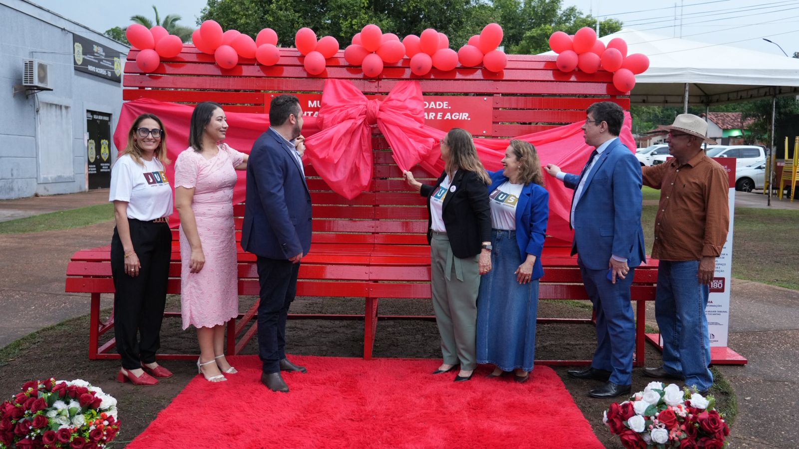 Sete pessoas, autoridades, seguram um grande laço vermelho simbolizando a inauguração do grande banco vermelho