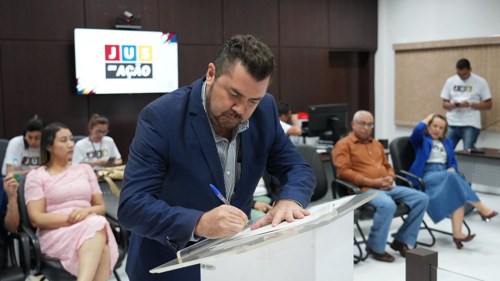 Prefeito de Novo Acordo; ele está usando terno azul e assina um documento