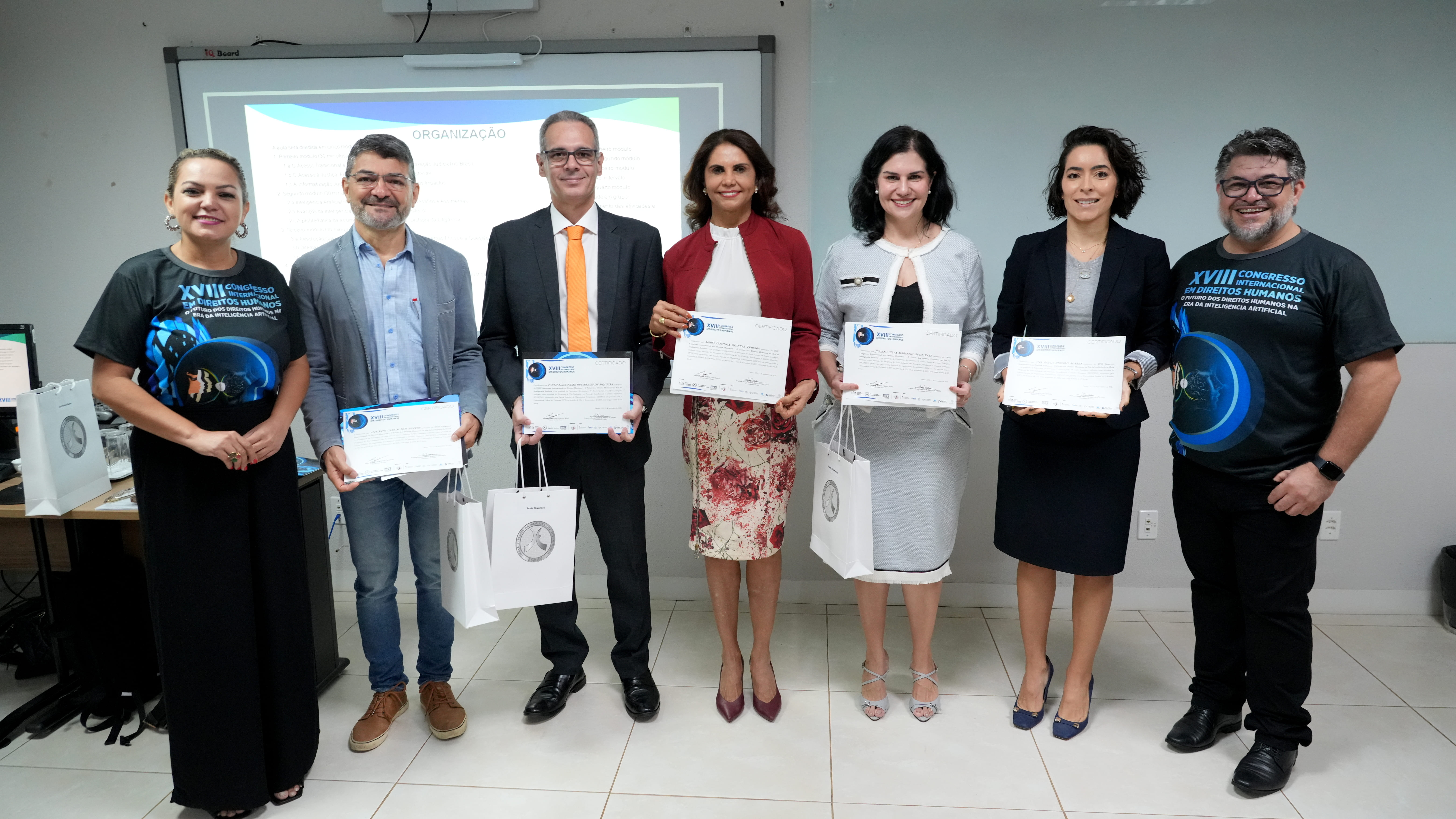 Grupo posa para foto após entrega de certificados durante evento institucional, com participantes segurando certificados e lembranças.