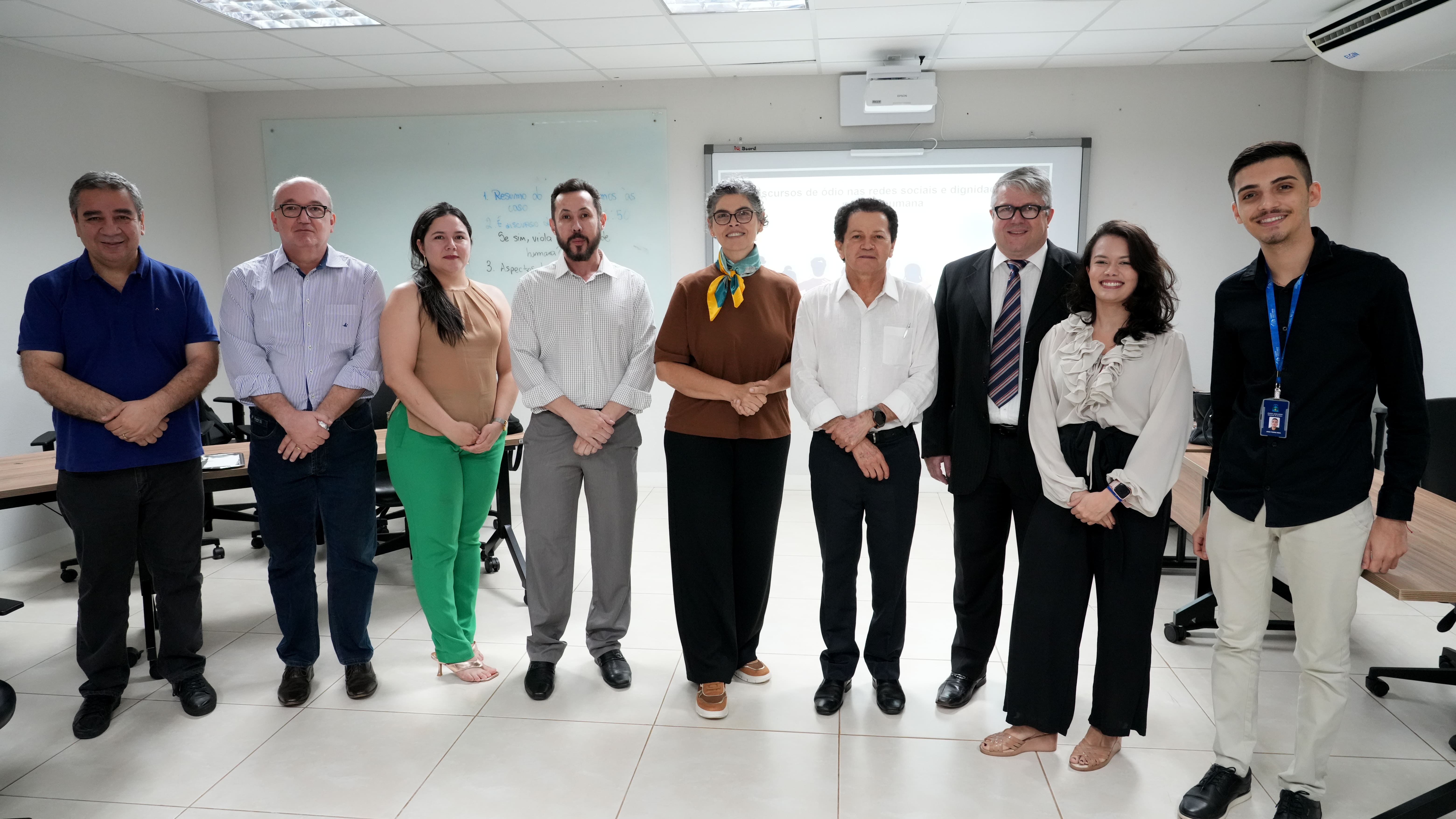 Grupo de pessoas posa para foto em sala de reunião, em ambiente institucional, após atividade ou encontro de trabalho.