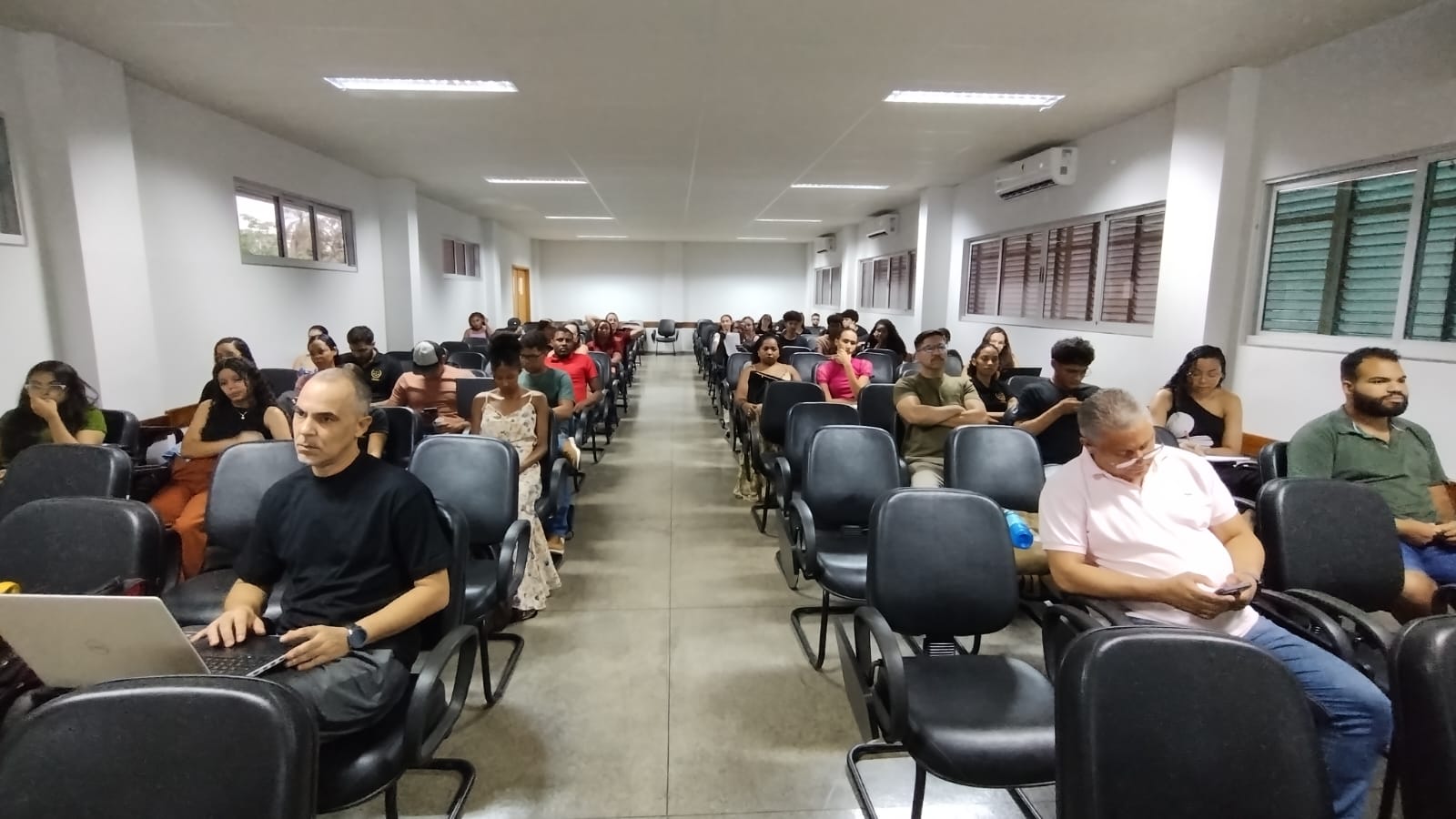 Foto aberta de um auditório e várias pessoas assistindo 