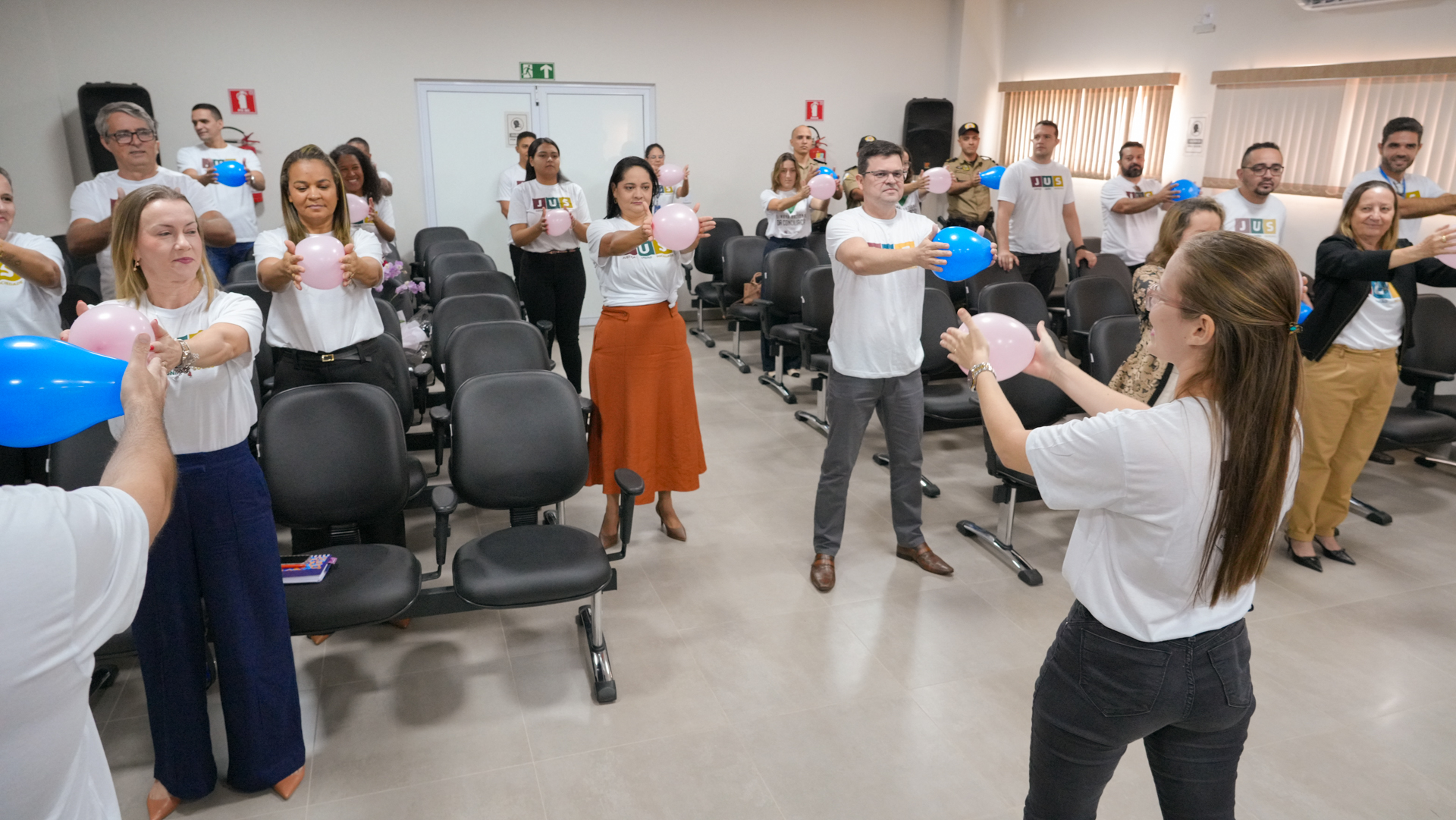Atividade coletiva com servidores do Judiciário durante ação institucional: participantes, em pé entre as cadeiras do auditório, realizam dinâmica de integração com balões, seguindo orientação de uma facilitadora.
