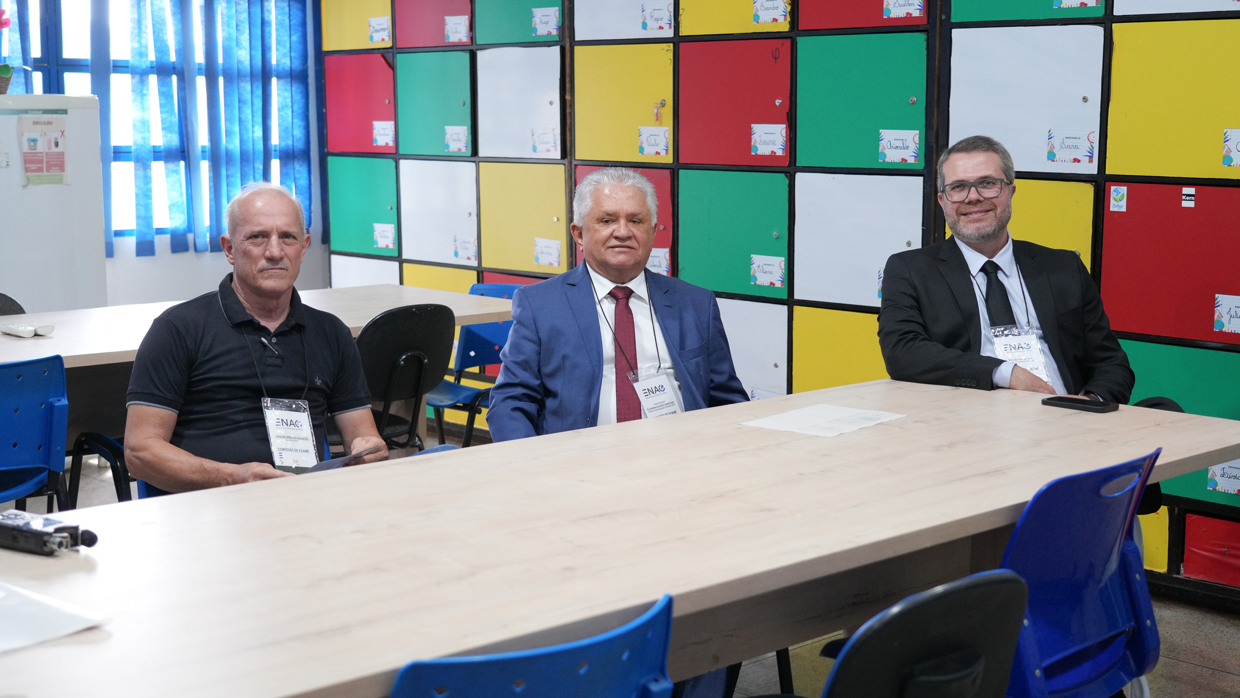 Três homens sentados em volta de uma mesa em uma sala com armários coloridos.