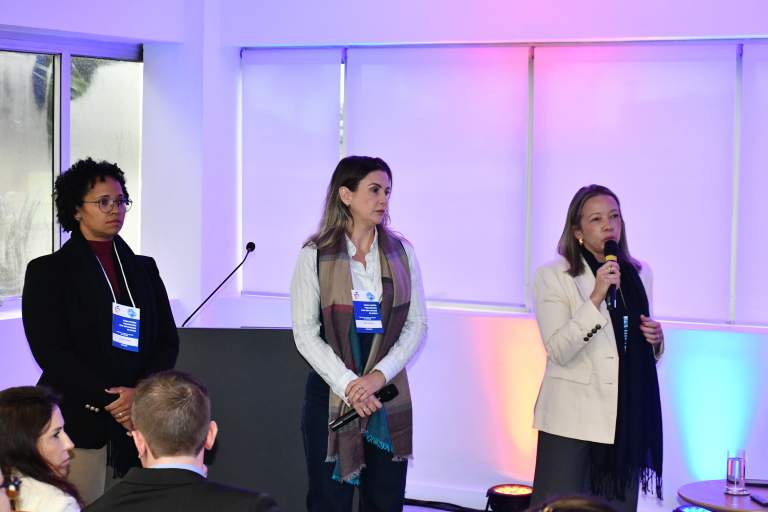 Três servidoras do TJTO em pé, durante capacitação; uma dela, da direita, fala ao microfone