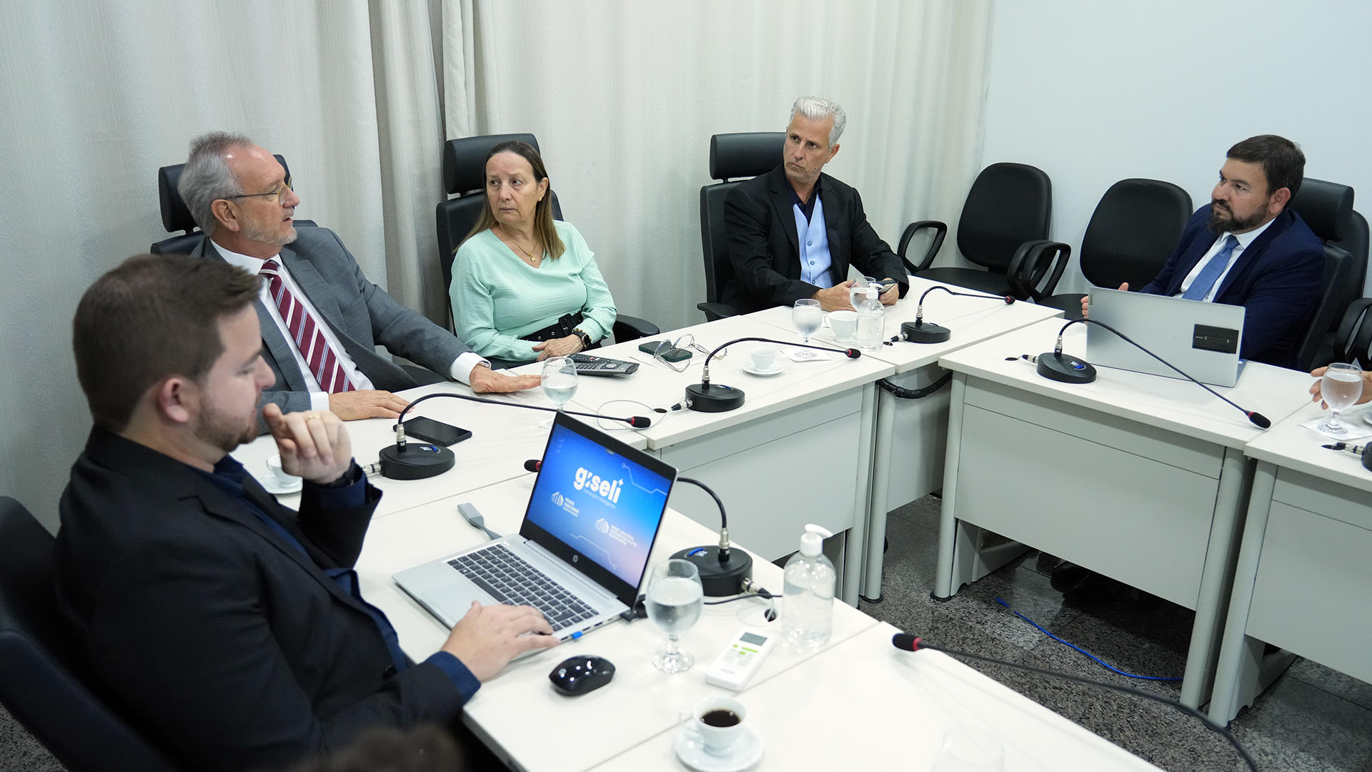 Desembargadores, servidores e consultor sentados em volta de uma mesa em formato U para apresentação de projeto