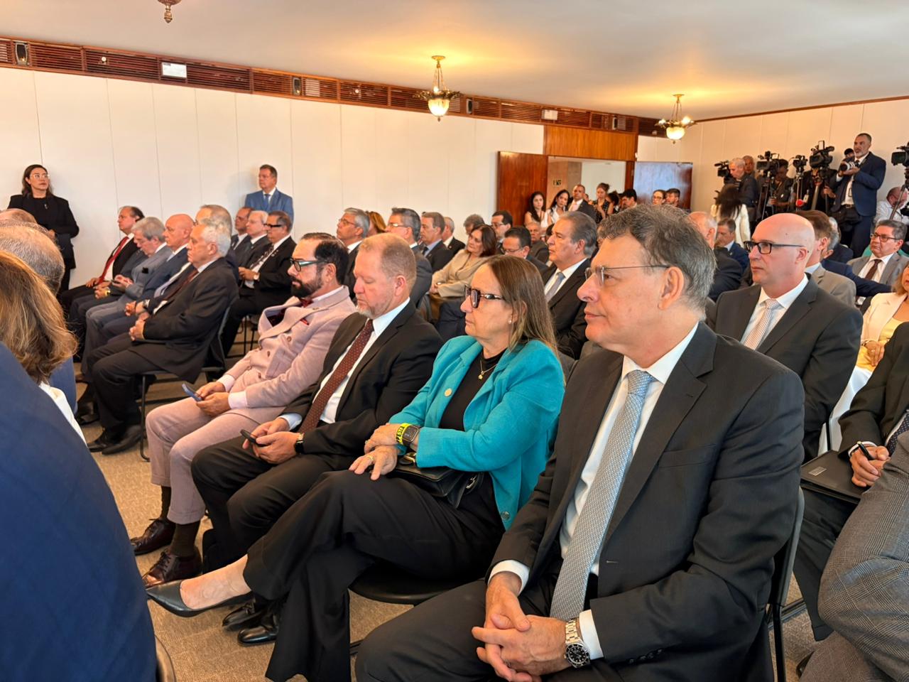 Autoridades acompanham evento institucional em auditório. Na fileira, destaca-se a desembargadora Maysa Vendramini Rosal, presidente do Tribunal de Justiça do Tocantins, vestindo blazer azul, sentada entre magistrados e convidados. Ao fundo, equipes de imprensa registram a solenidade com câmeras e equipamentos de filmagem.