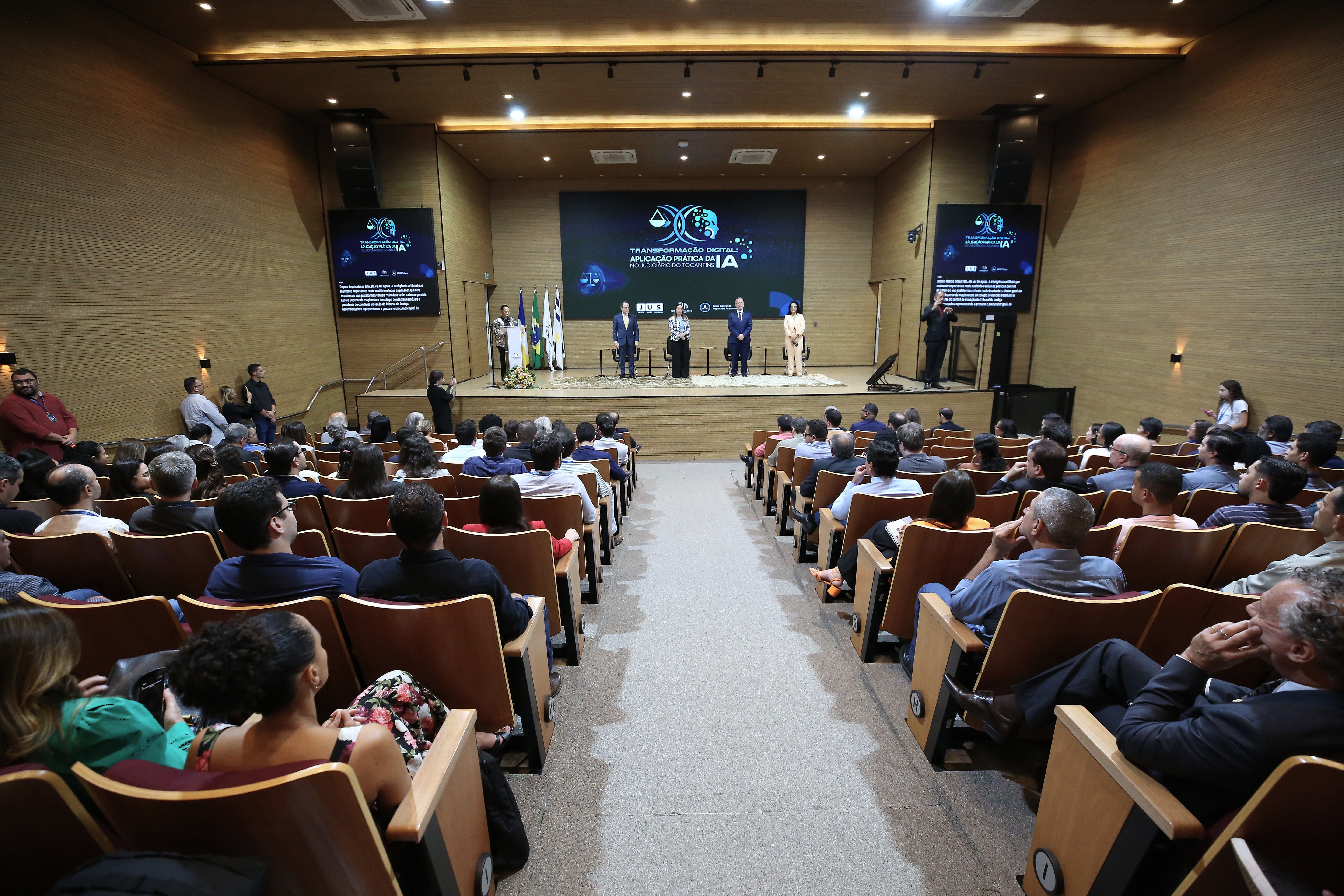 A imagem mostra o auditório do Tribunal de Justiça do Tocantins lotado durante a abertura do evento “Transformação Digital: Aplicação Prática da IA no Judiciário do Tocantins”, com autoridades no palco e público atento.