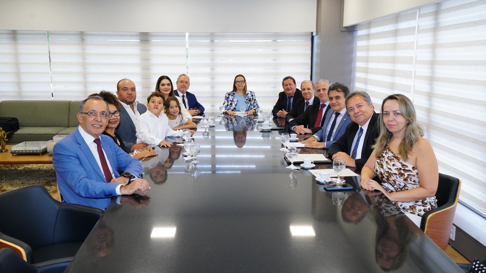 A imagem mostra autoridades do Judiciário e familiares reunidos em torno de uma mesa durante a cerimônia de posse da juíza Ana Priscila da Cruz Dias, realizada no gabinete da Presidência do TJTO. O registro marca o momento histórico da primeira permuta interestadual de magistrados(as) no Judiciário tocantinense.