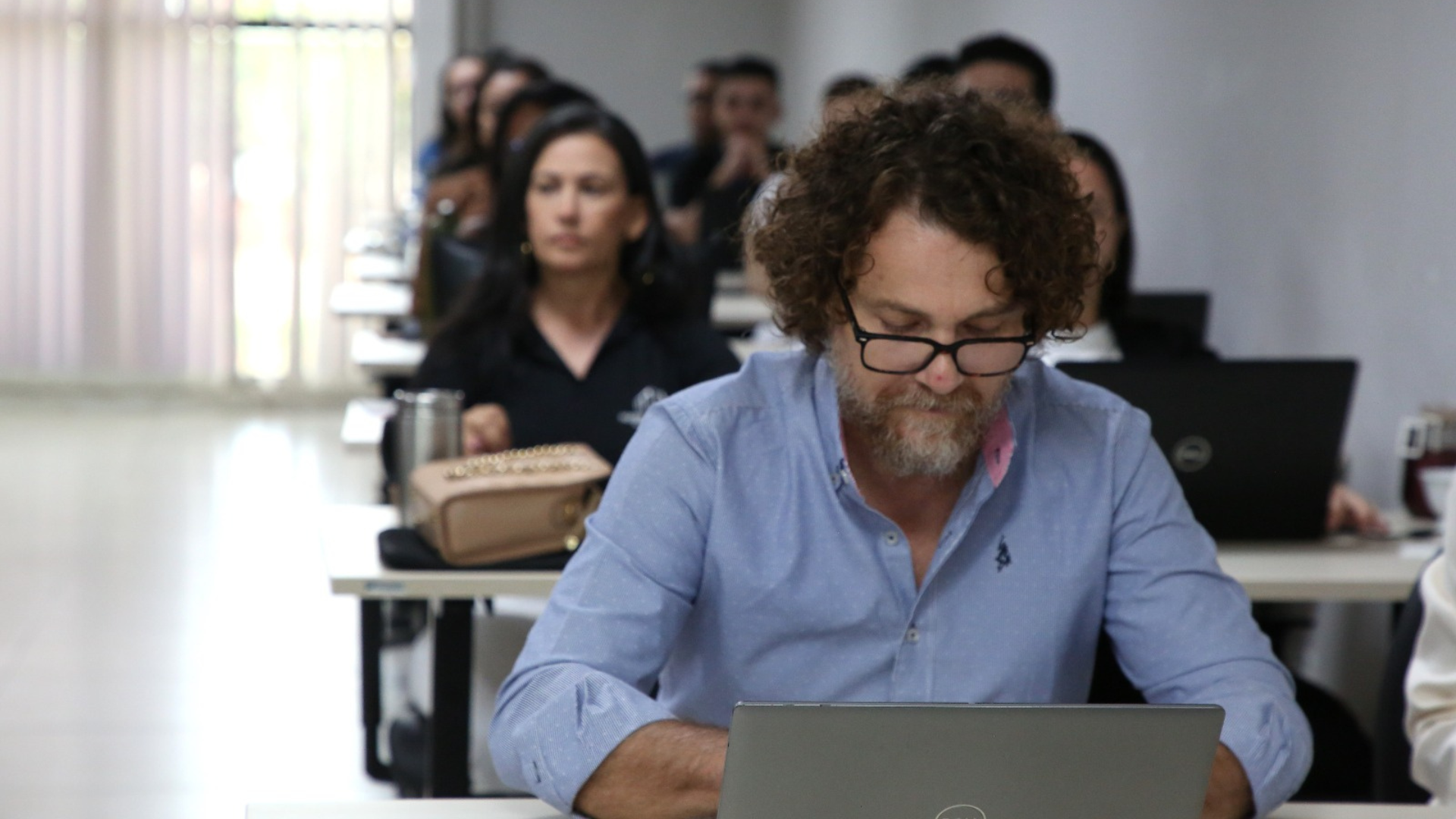 A imagem mostra participantes durante curso de crédito rural, reunidos em sala de capacitação e utilizando notebooks para acompanhamento das atividades.  Em primeiro plano, um participante acompanha atentamente o conteúdo no computador, enquanto outros alunos aparecem ao fundo.