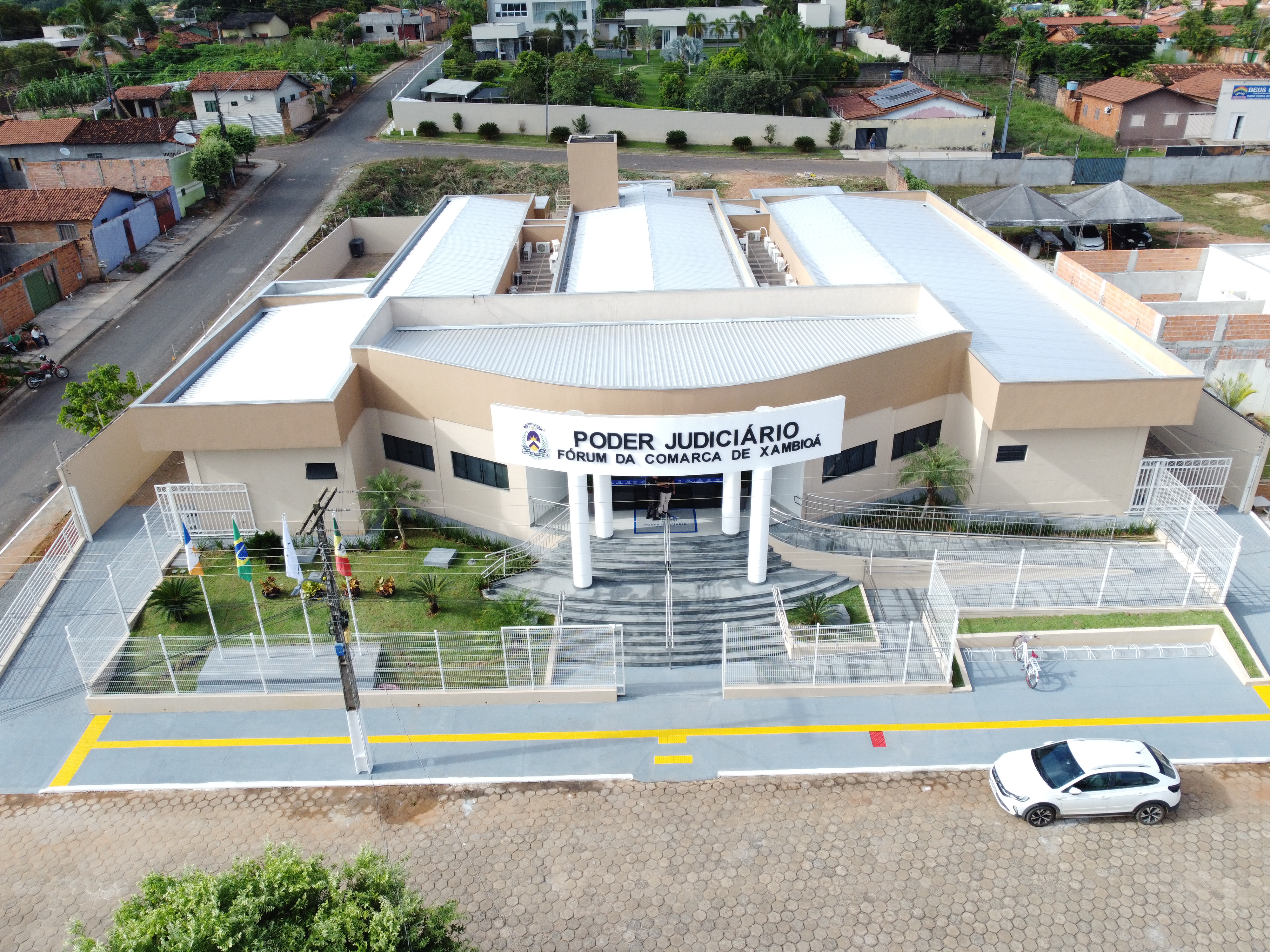 A imagem mostra vista aérea do Fórum da Comarca de Xambioá após reforma, com fachada moderna, estrutura acessível e área externa cercada. Ao redor, aparecem ruas residenciais, casas e vegetação, evidenciando a integração da unidade ao contexto urbano da cidade.