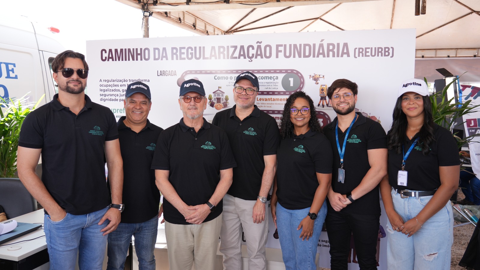A imagem mostra equipe da Corregedoria da Justiça com 7 pessoas em pé, posando para foto no espaço de atendimento da Regularização Fundiária (Reurb) durante a Agrotins 2026.