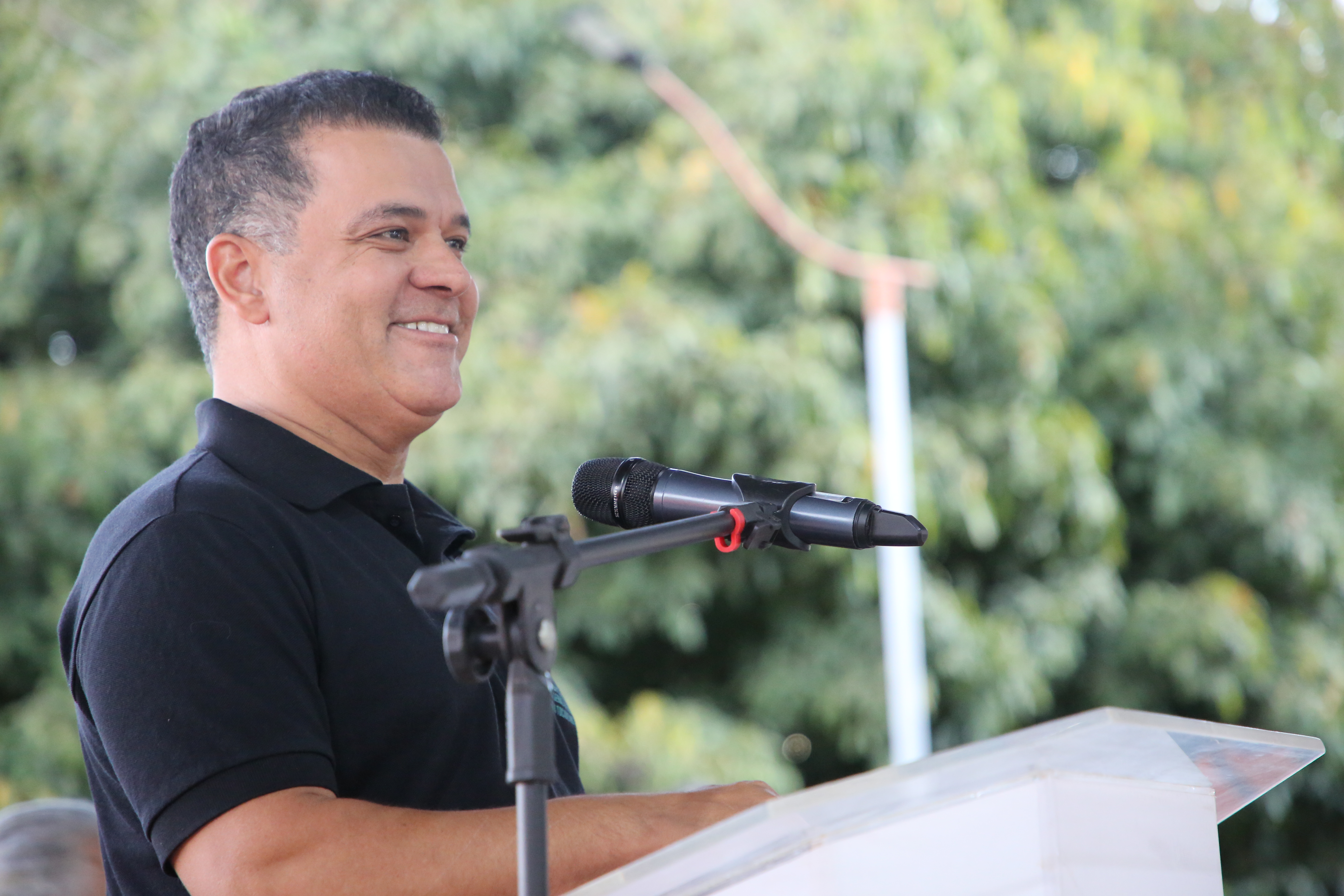 Juiz Jordan Jardim durante discurso no evento Solo Seguro, em pé atrás de um púlpito e ao microfone, com expressão sorridente. A imagem tem ao fundo árvores desfocadas e ambiente ao ar livre.