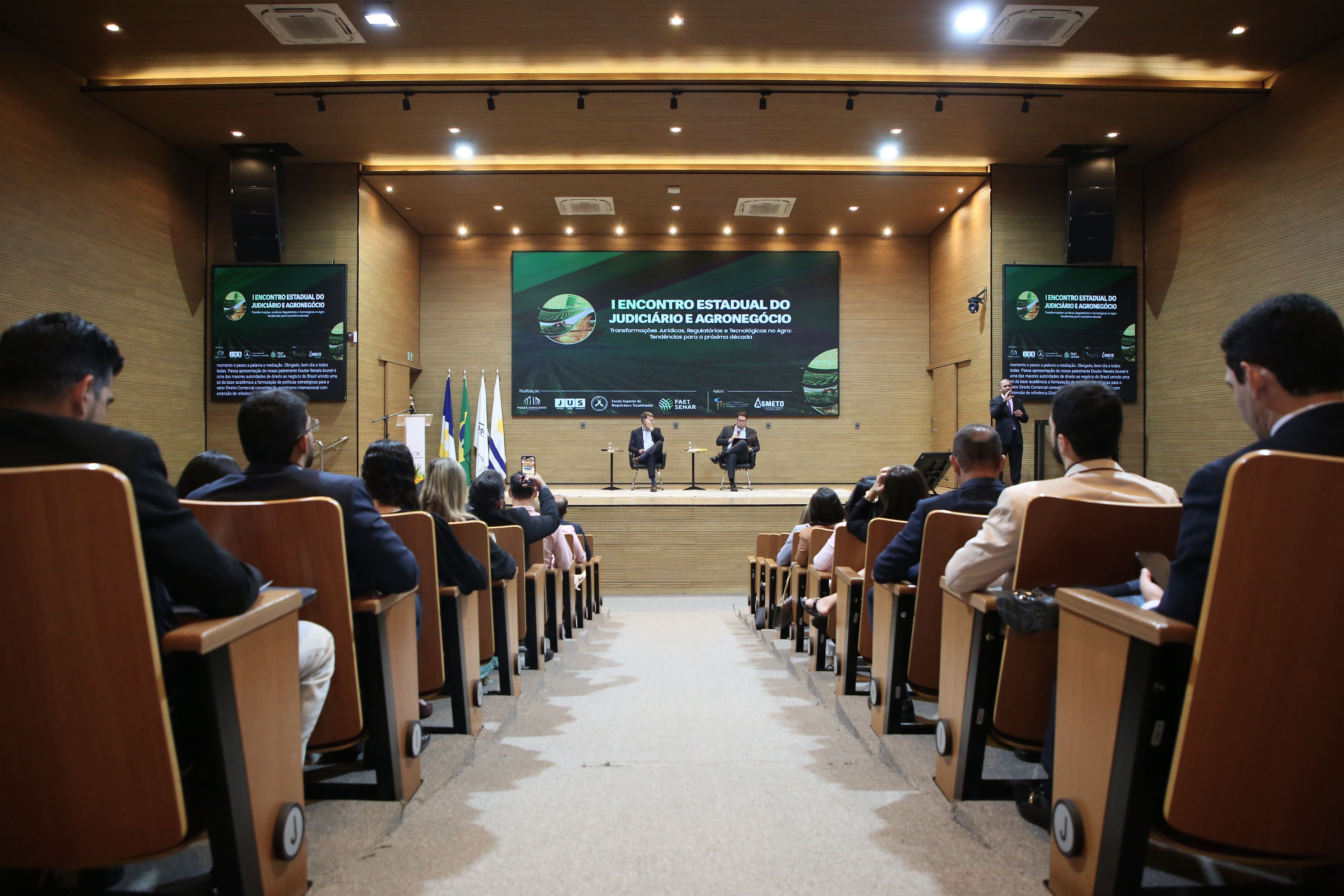 A imagem mostra o auditório do TJTO durante o I Encontro Estadual do Judiciário e Agronegócio, com participantes acompanhando um painel de debates no palco.