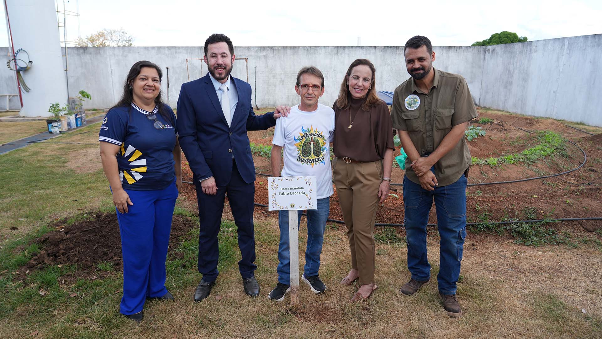 Imagem mostra autoridades e servidor homenageado em frente a horta mandala
