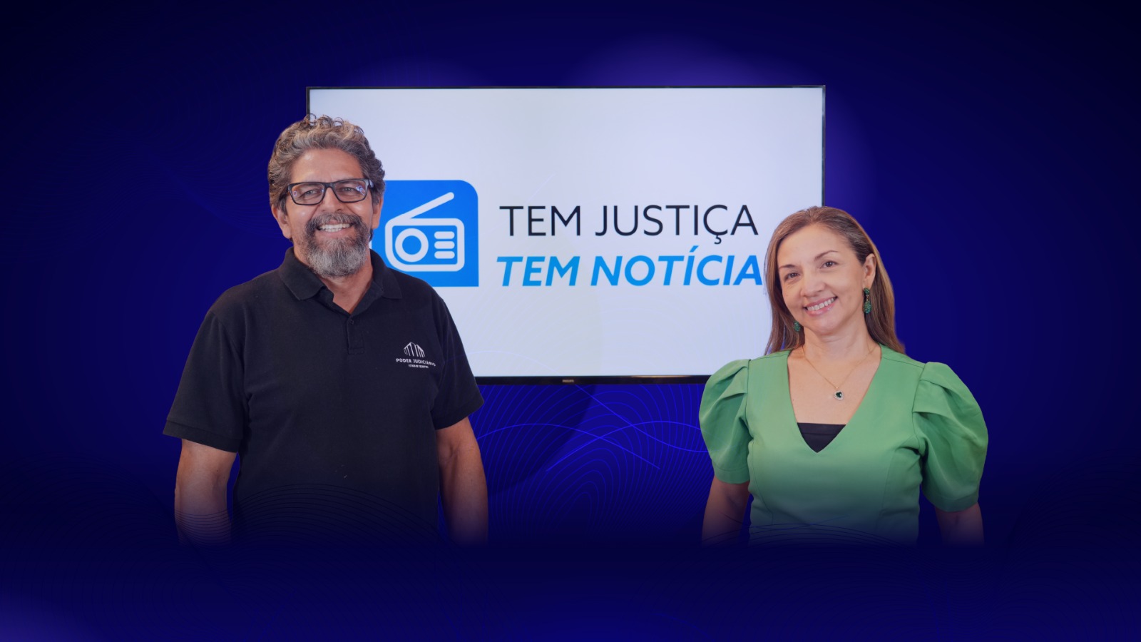 Os jornalistas Lailton Costa e Neuracy Viana posam no estúdio do programa de rádio “Tem Justiça, Tem Notícia”, diante de um painel com a identidade visual da atração. Com sorrisos e postura acolhedora, os apresentadores representam a proposta do programa de aproximar o Poder Judiciário da população por meio de informação acessível, prestação de serviço e cidadania. O ambiente conta com fundo em tons de azul.