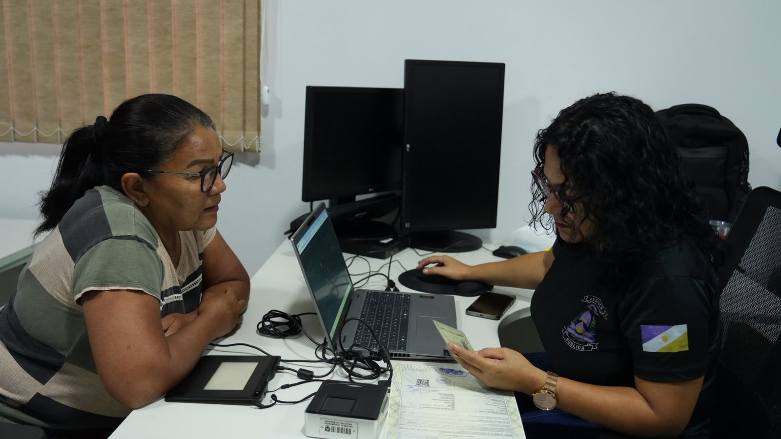 Dona Edivan é atendida durante o mutirão do projeto JUS em Ação para a emissão de documento de identificação. Na imagem, ela apresenta a documentação necessária enquanto recebe orientações de uma servidora responsável pelo atendimento, em uma ação que amplia o acesso da população aos serviços essenciais de cidadania.