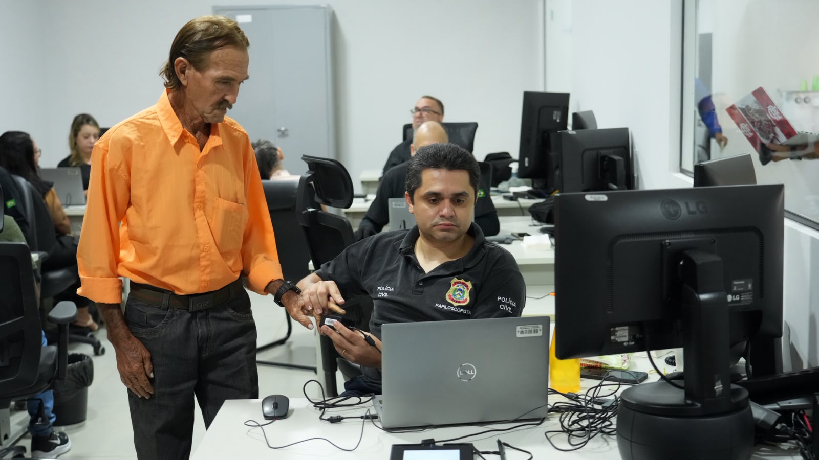 Seu Raimundo é atendido durante o mutirão do projeto JUS em Ação para a emissão de documento de identificação. Na imagem, ele recebe orientação de um servidor da Polícia Civil, responsável pelo cadastro e coleta de dados, em uma das estações de atendimento montadas para facilitar o acesso da população aos serviços de cidadania.