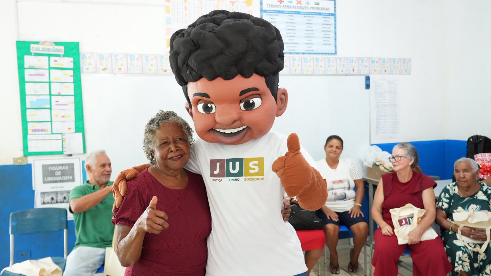 Dona Raimunda participa da oficina voltada à pessoa idosa durante o projeto JUS em Ação. Ao lado do mascote Justino, ela registra um momento de alegria e descontração durante a atividade, que promoveu informação, convivência e valorização da população idosa, fortalecendo o exercício da cidadania e o acesso aos direitos.