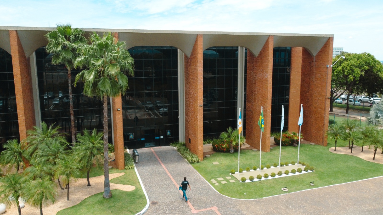 A imagem mostra a fachada principal do Tribunal de Justiça do Tocantins, em Palmas, cercada por jardins, palmeiras e mastros com bandeiras institucionais.