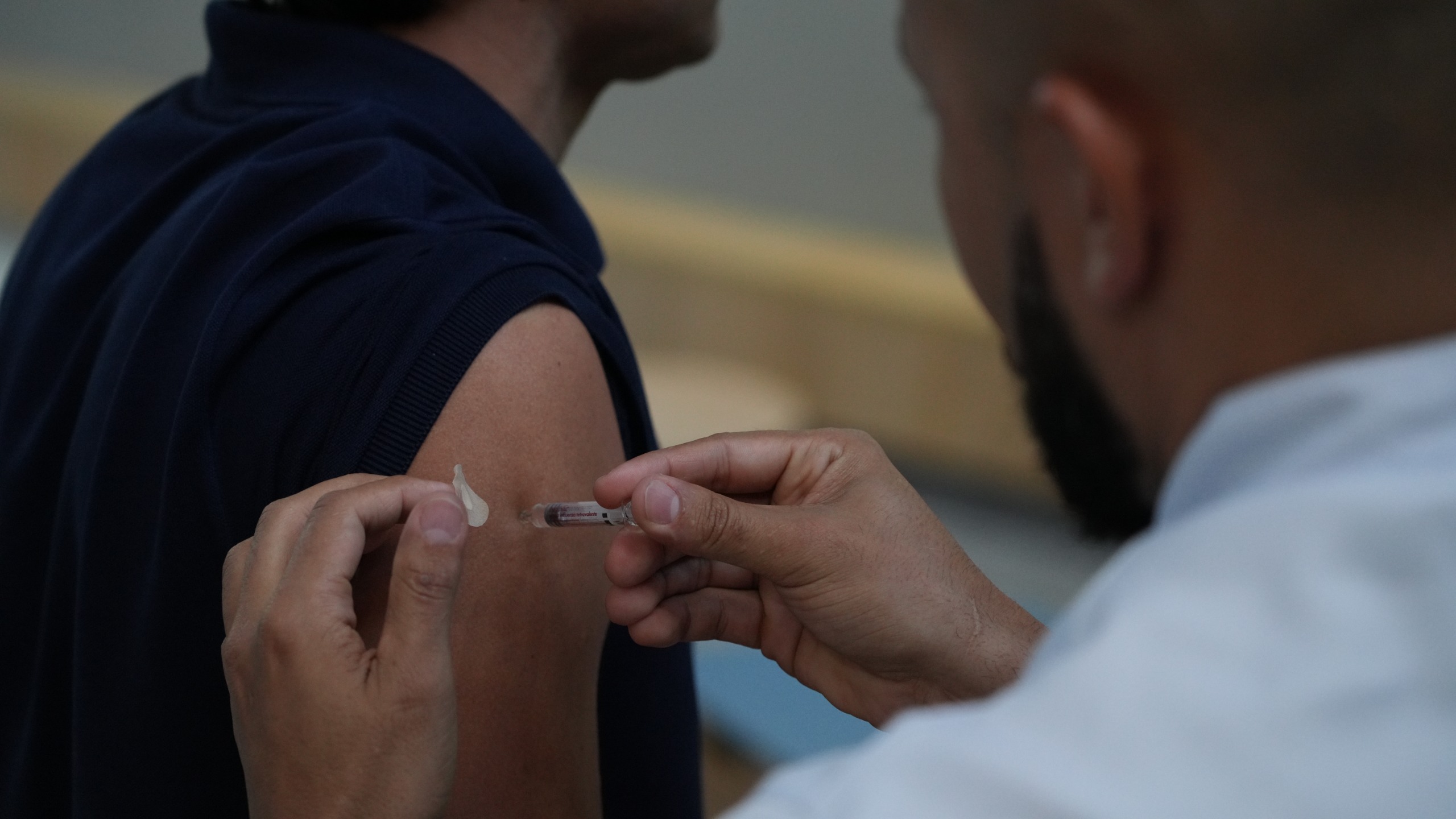 A imagem mostra um profissional de saúde aplicando uma dose de vacina em um homem.