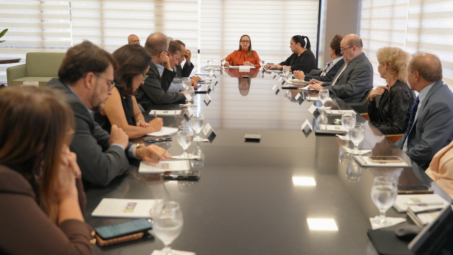 A imagem mostra diversas autoridades, magistrados(as), gestores(as) e equipes técnicas sentados ao redor de uma longa mesa de reuniões na sala da Presidência do Tribunal de Justiça do Tocantins, durante a apresentação do Programa de Transformação Digital e dos projetos de Inteligência Artificial do TJTO.