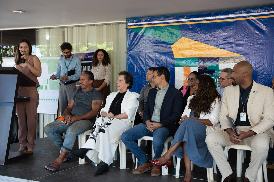 A imagem registra um momento da solenidade de lançamento do Espaço Aroeira – Cidadania PopRua Palmas. À esquerda, uma mulher faz uso da palavra em um púlpito, dirigindo-se aos participantes e convidados presentes no evento.  Ao centro e à direita, autoridades, representantes de instituições parceiras e integrantes da comunidade acompanham atentamente o discurso. Entre os presentes, destacam-se membros do Poder Judiciário, do sistema de justiça e representantes da população em situação de rua, simbolizando o caráter inclusivo da iniciativa.