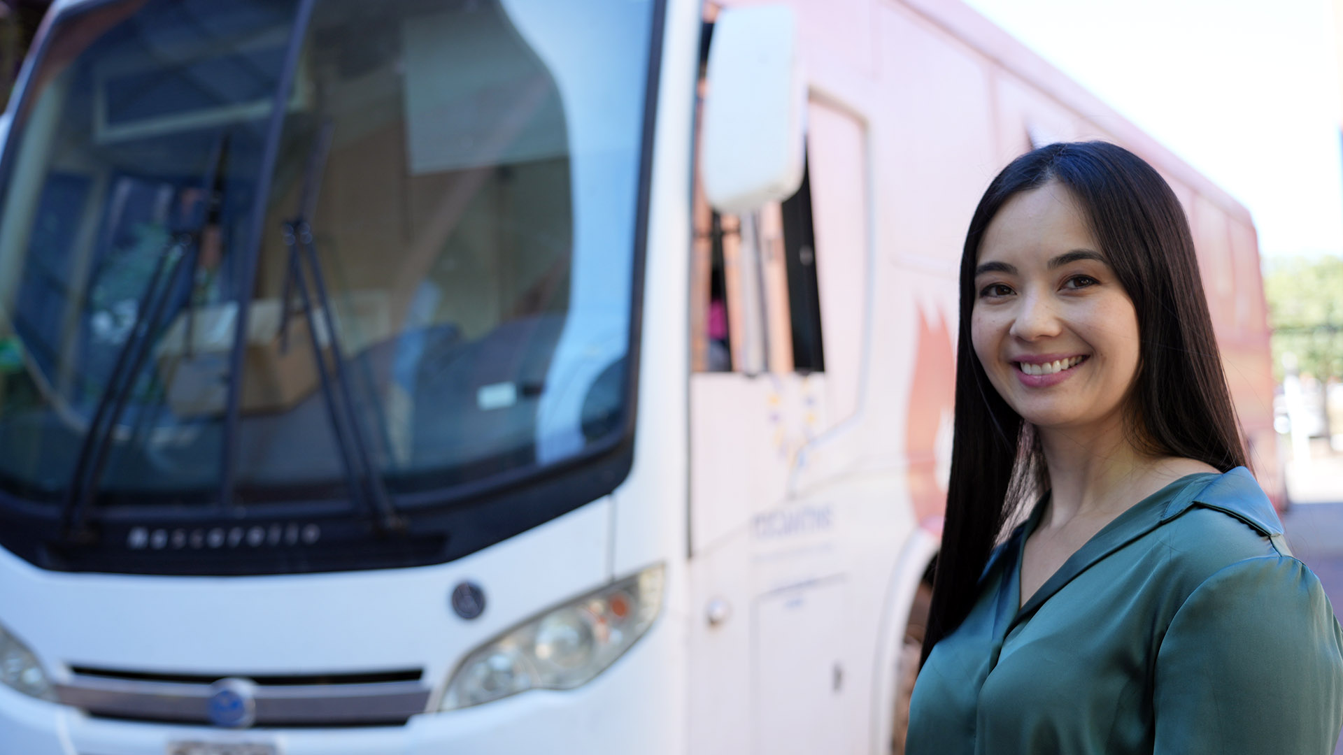 A imagem mostra uma mulher sorrindo, posicionada ao lado da unidade móvel do Hemocentro, utilizada para a campanha de doação de sangue realizada no Tribunal de Justiça do Tocantins.