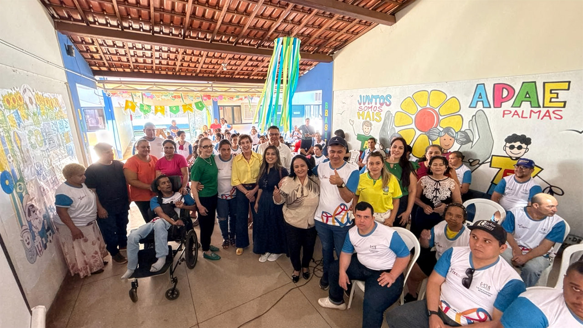 A presidente da Comissão Permanente de Acessibilidade e Inclusão (CPAI) do Tribunal de Justiça do Tocantins, desembargadora Angela Haonat, a secretária executiva da comissão, Patrícia Idehara, representantes da Apae de Palmas, estudantes, familiares e colaboradores reúnem-se para registro durante o 1º Festival TEAtivo – Copa do Mundo, realizado na sede da instituição. Ao fundo, o mural da Apae Palmas reforça a mensagem de inclusão e acolhimento que marcou o evento.  Legenda jornalística: