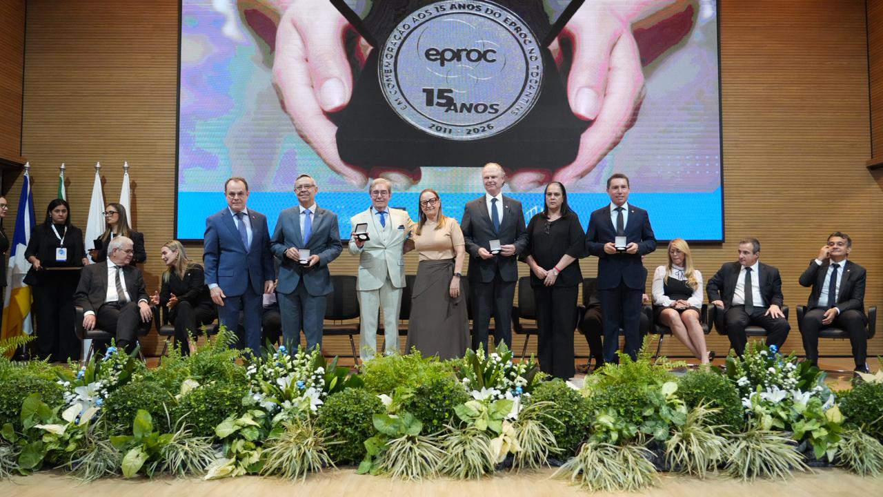 Autoridades e representantes de tribunais brasileiros posam para foto no palco do auditório do Tribunal de Justiça do Tocantins durante a cerimônia de abertura do IV Encontro Interinstitucional do eproc. Ao centro, os homenageados exibem as medalhas comemorativas entregues em celebração aos 15 anos de implantação do eproc no Judiciário tocantinense. Ao fundo, um painel destaca a marca alusiva à data comemorativa.