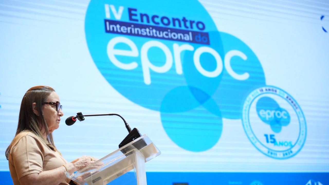 Desembargadora Maysa fala ao microfone; ao fundo um painel de LED com o nome: IV Encontro Interinstitucional do eproc