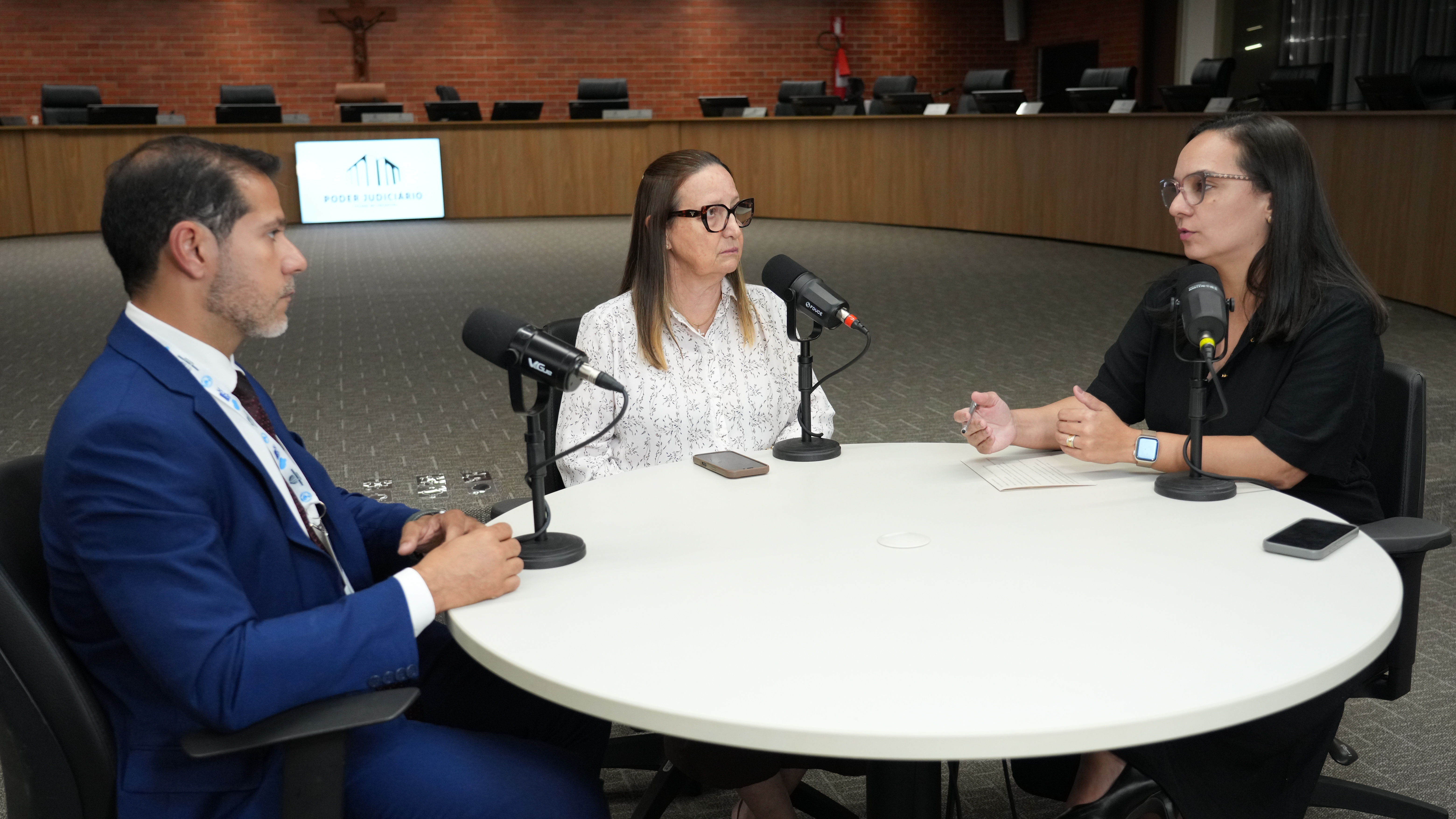 A jornalista Paula Bittencourt conduz a gravação de um episódio da segunda temporada do podcast Conexão JUS, com a participação do analista judiciário Ângelo Stacciarini Seraphin e da presidente do Tribunal de Justiça do Tocantins, desembargadora Maysa Vendramini Rosal. Reunidos em torno de uma mesa equipada com microfones, os convidados debatem as perspectivas e os desafios que devem orientar o futuro da comunidade eproc e a evolução do sistema nos próximos anos.
