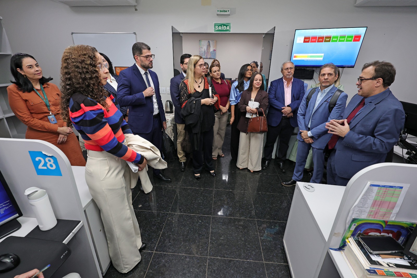 A imagem mostra integrantes da comitiva do TJTO durante visita técnica a uma Central de Processamento Eletrônico, acompanhando a apresentação sobre a organização e os fluxos de trabalho da unidade.  Reunidos no ambiente da CPE, magistrados(as) e servidores(as) observam as boas práticas adotadas pelo tribunal visitado, em momento de intercâmbio de experiências voltado ao aprimoramento da prestação jurisdicional.
