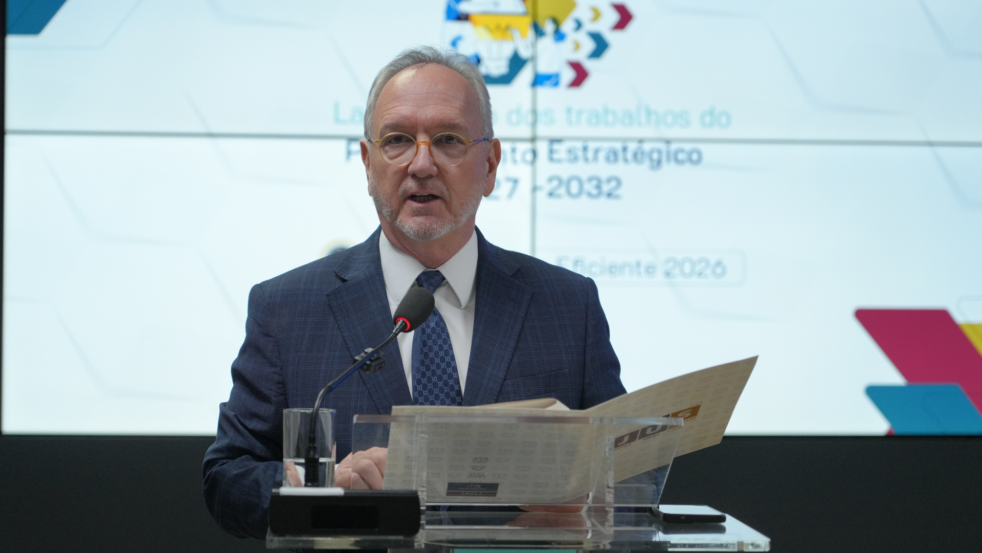 O desembargador Pedro Nelson de Miranda Coutinho aparece em pé, fazendo uso da palavra ao microfone durante a abertura dos trabalhos de construção do Planejamento Estratégico 2027–2032. Ao fundo, o telão exibe a identidade visual do evento.