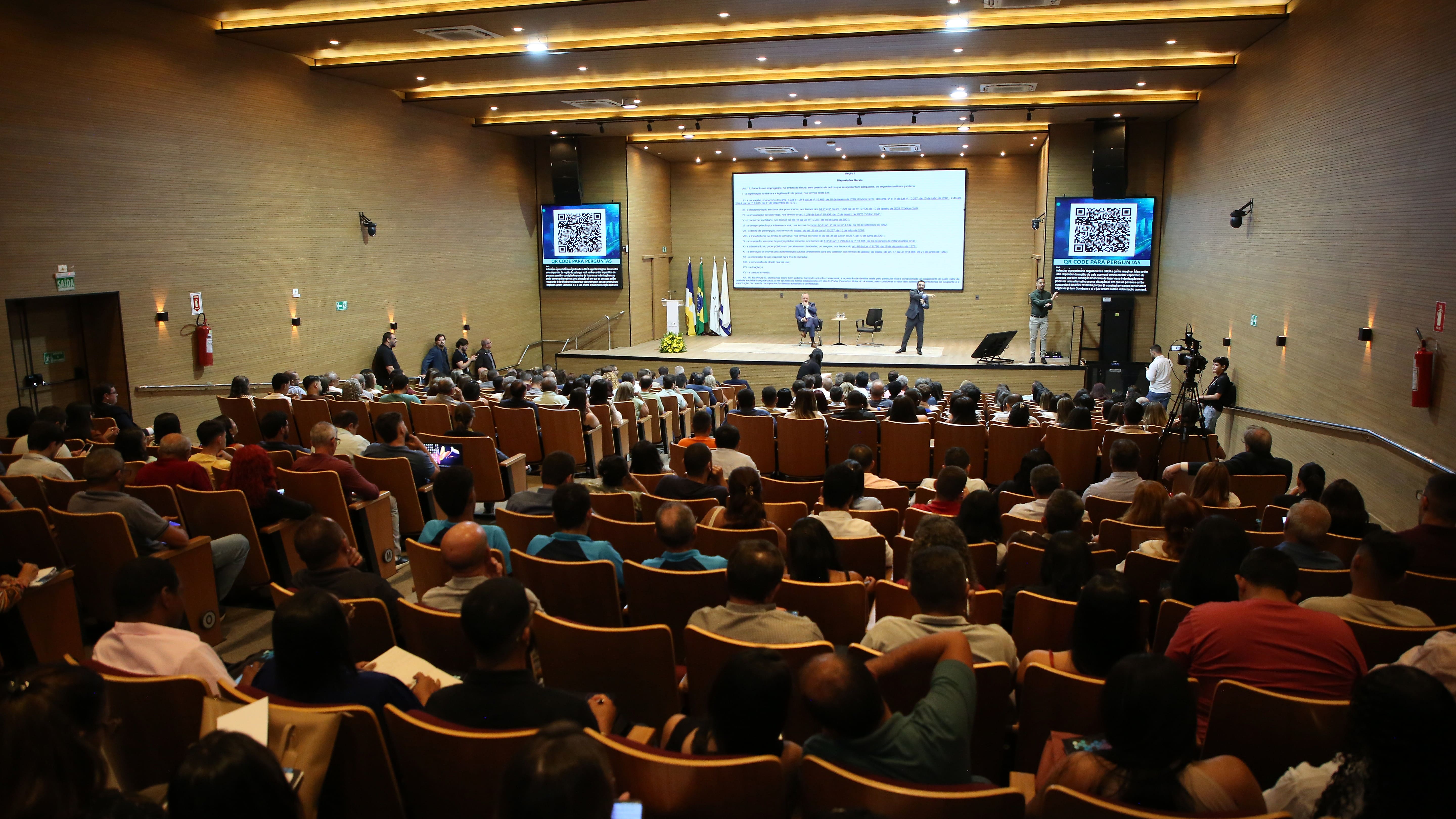 A imagem mostra participantes reunidos no auditório do TJTO durante o primeiro dia do III Fórum Fundiário do Tocantins. Ao fundo, palestrantes conduzem a programação do evento, acompanhada pelo público presente.