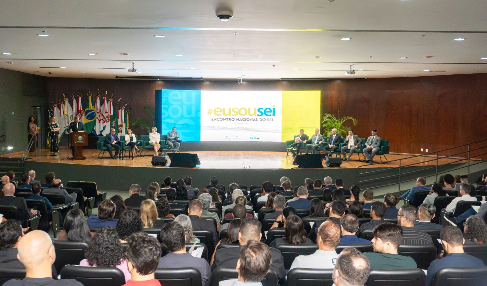A imagem mostra a cerimônia de abertura do Encontro Nacional do SEI 2026, com autoridades e convidados no palco e o painel oficial do evento ao fundo. Na plateia, participantes acompanham a programação realizada em Brasília.