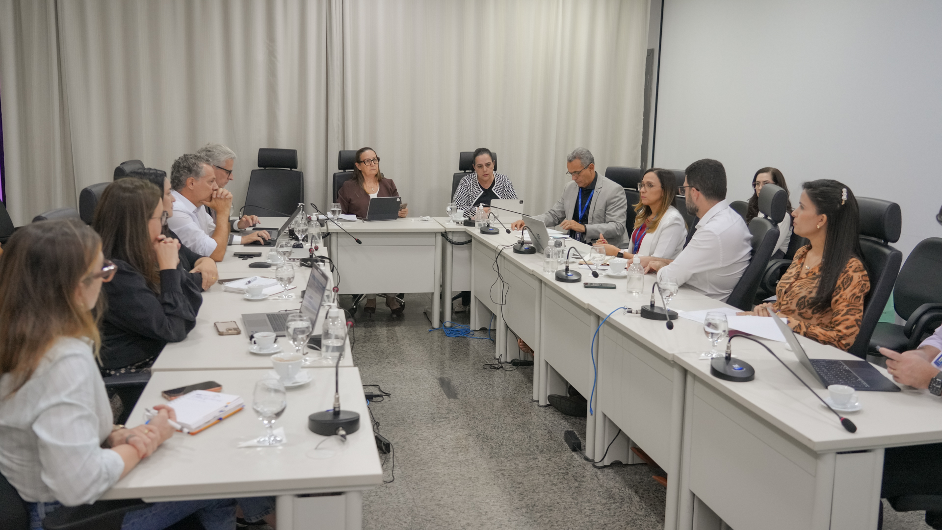Reunião de trabalho reúne magistrados(as) e servidores(as) em uma sala institucional, organizados em torno de mesa em formato de U