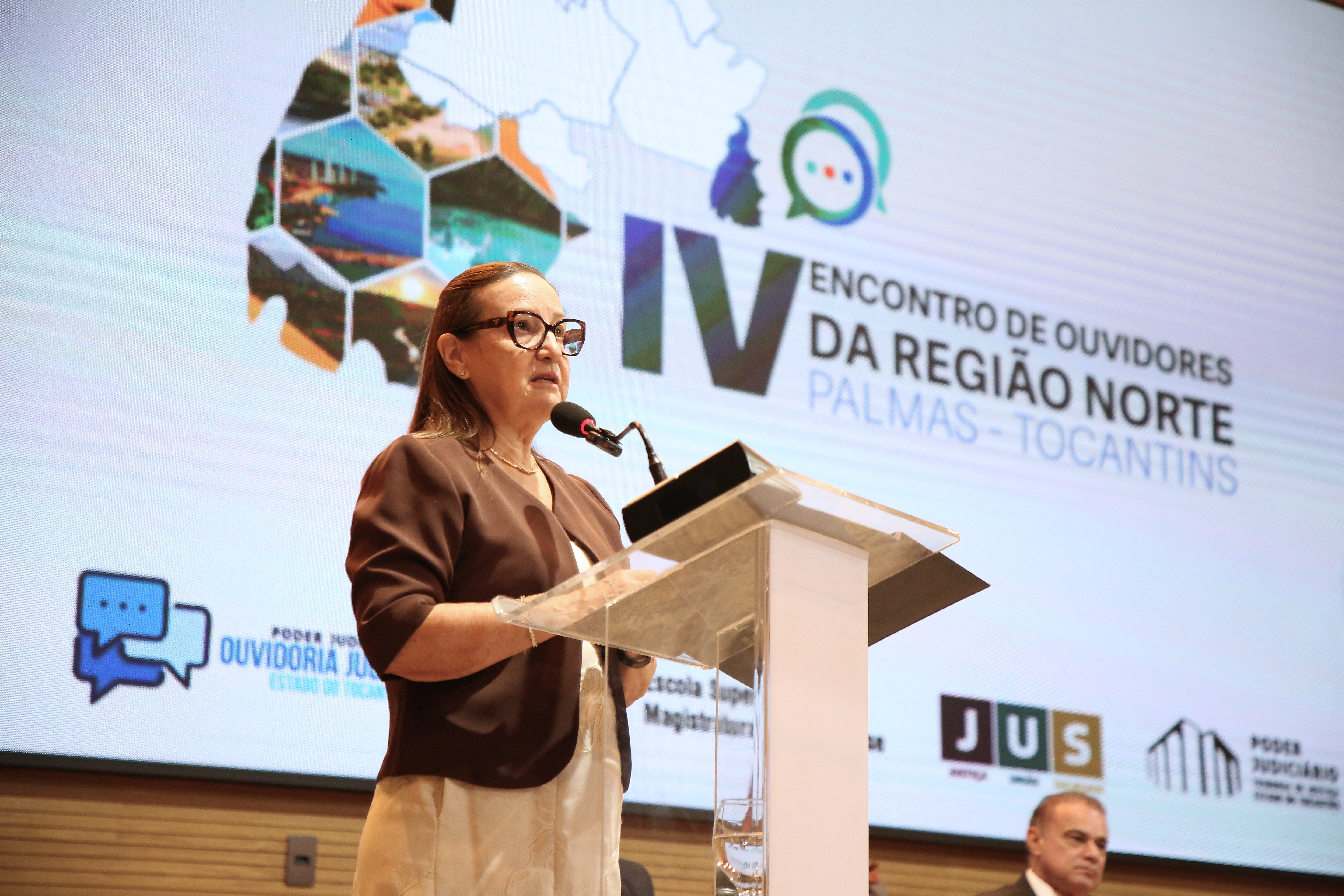 A presidente do Tribunal de Justiça do Tocantins (TJTO), desembargadora Maysa Vendramini Rosal, discursa em púlpito durante o IV Encontro de Ouvidores e Ouvidoras Judiciais da Região Norte. Ao fundo, o painel oficial do evento.