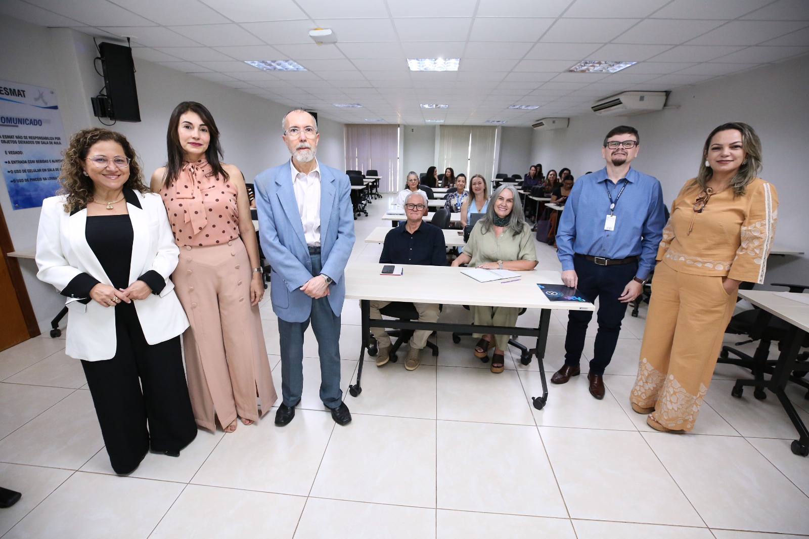 Foto registra cinco pessoas em pé em uma sala de aula da Esmat, enquanto outros participantes acompanham a atividade ao fundo