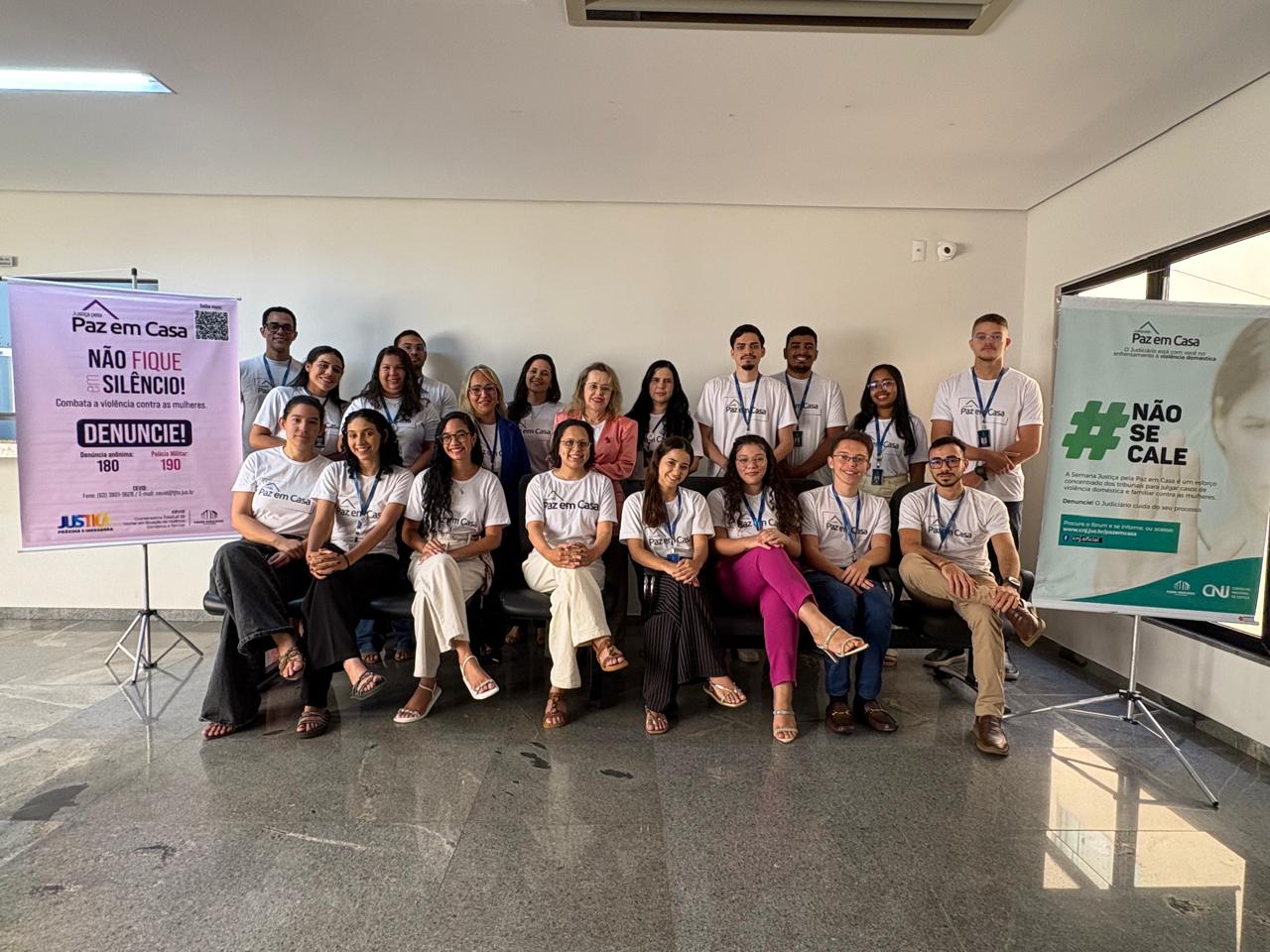Equipe da Comarca de Araguaína posa para foto em ambiente interno, entre banners da campanha Justiça pela Paz em Casa. A maioria dos integrantes veste camisetas da mobilização, que reforça mensagens de conscientização, denúncia e enfrentamento à violência doméstica contra a mulher.