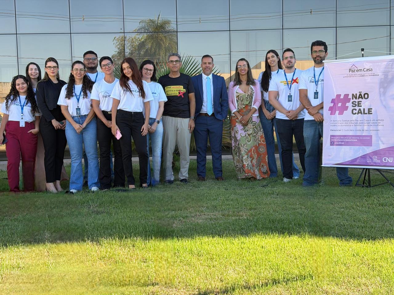 Equipe da Comarca de Gurupi posa para foto em área externa, em frente ao prédio da unidade judicial. Parte dos integrantes veste camisetas da campanha Justiça pela Paz em Casa. Ao lado do grupo, banner com a mensagem “#Não se Cale” reforça a conscientização e o enfrentamento à violência doméstica contra a mulher.