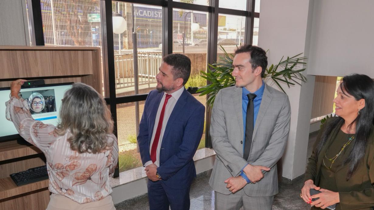 Em frente a um computador instalado em um móvel de madeira, uma mulher utiliza o sistema de reconhecimento facial exibido na tela. Ao lado, autoridades e representantes de instituições acompanham a demonstração do SAREF no Fórum de Araguaína.